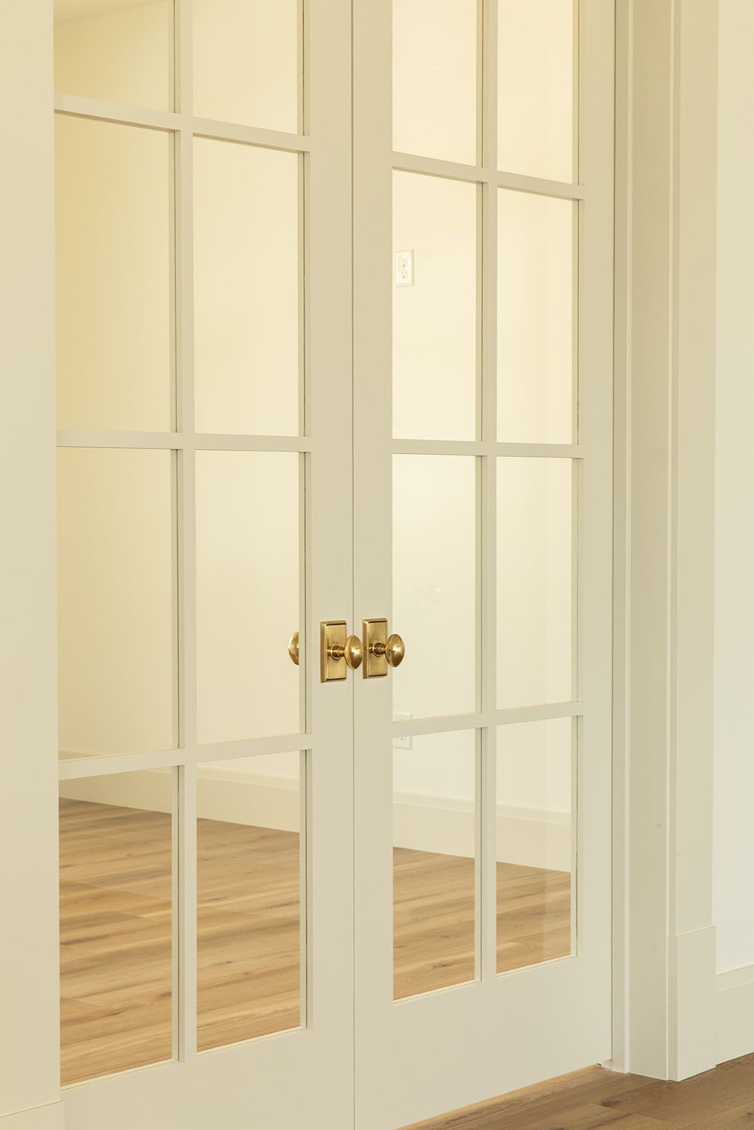 Elegant white French doors with glass panels and brass knobs opening to a bright room with hardwood floors.