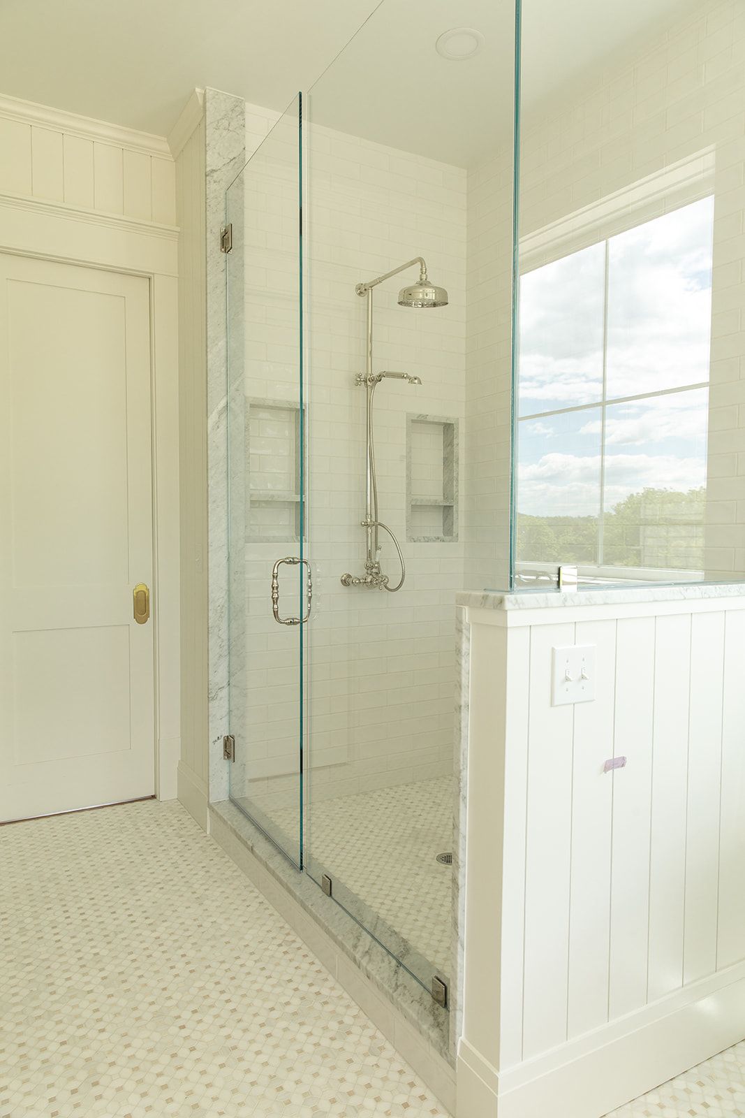 Glass-enclosed walk-in shower with rainfall showerhead, marble tile, and mosaic floor in a white shiplap bathroom.