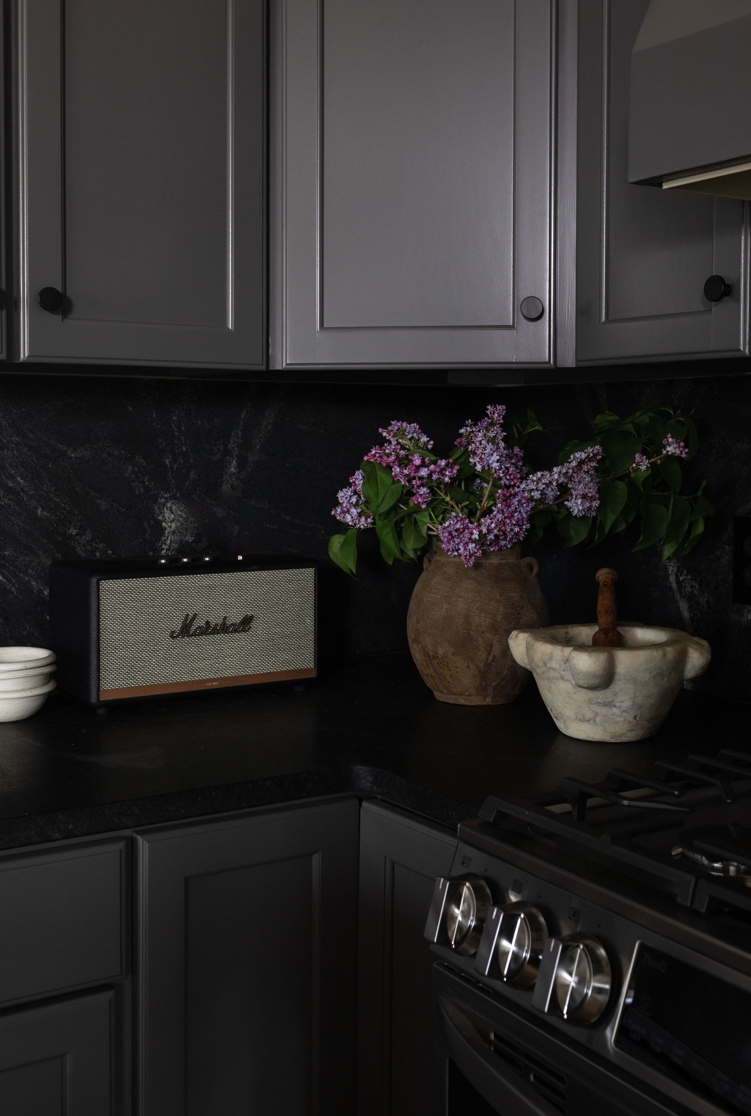 Dark moody kitchen with black cabinetry and purple flowers in rustic pots on the counter.