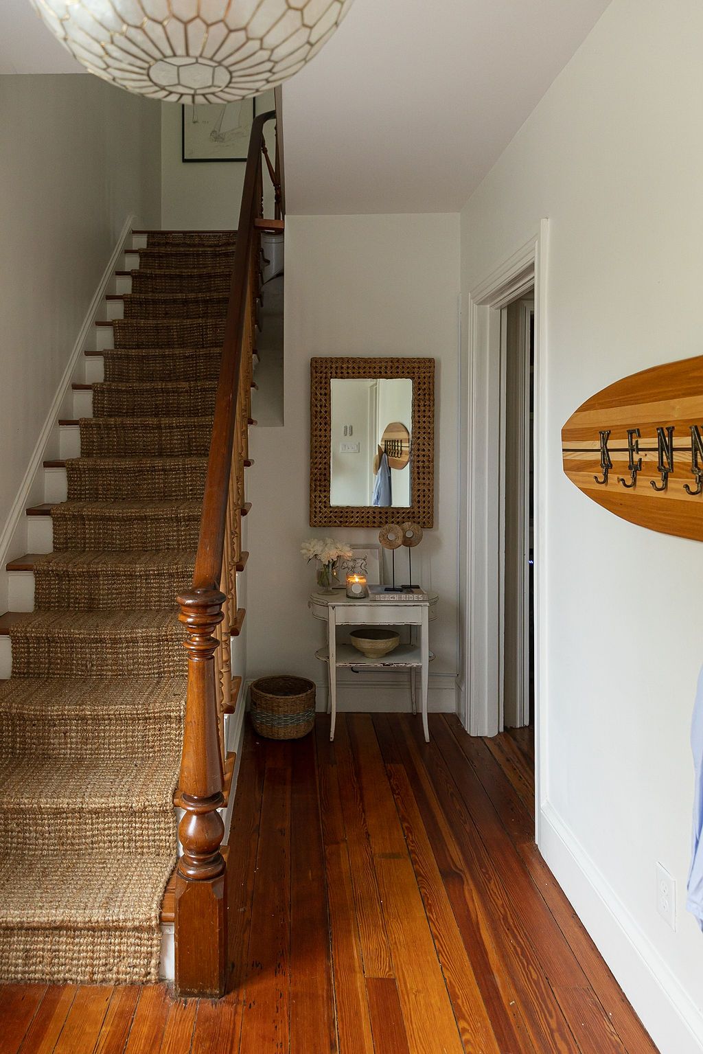 A coastal-style entryway features a sisal stair runner, hardwood floors, surfboard decor and a decorative wall mirror.