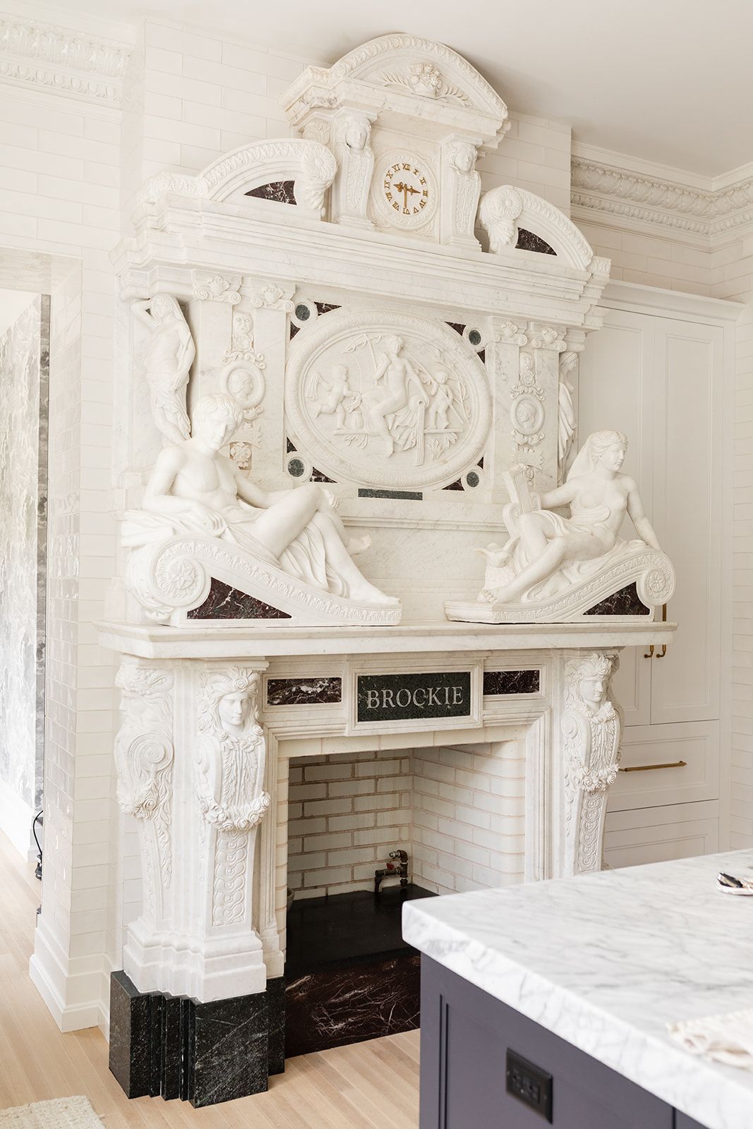 Elaborate white marble fireplace with classical sculptures and decorative reliefs in modern kitchen.