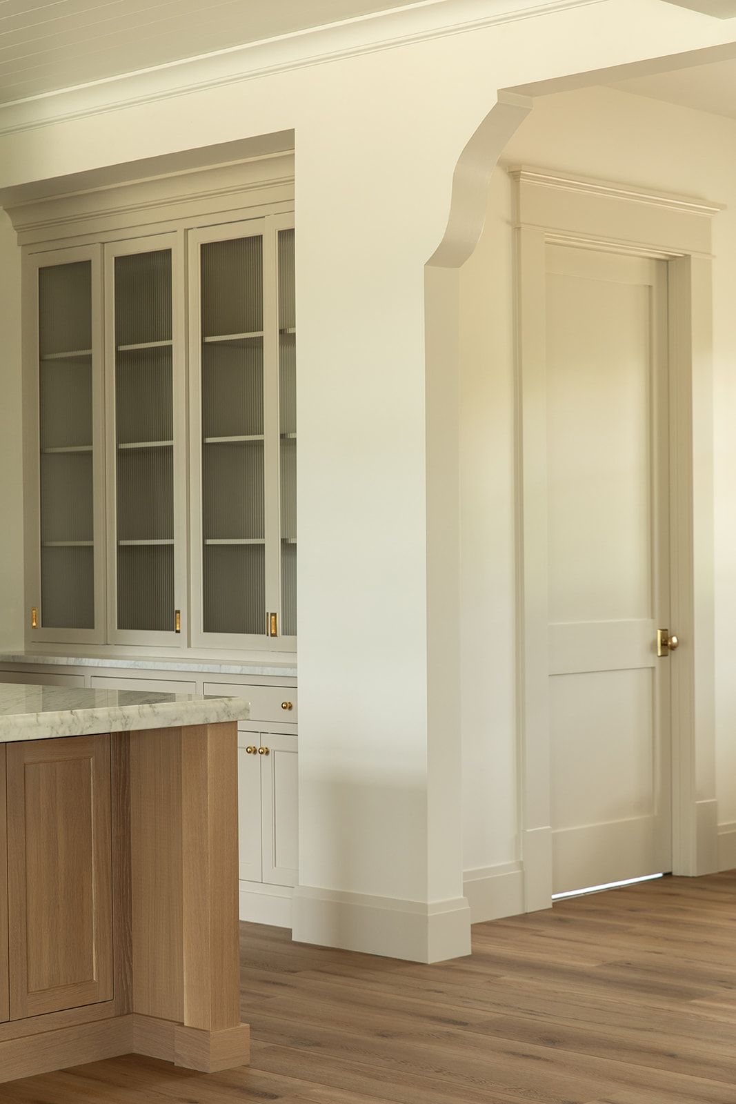 Classic kitchen featuring glass-front cream cabinets, brass hardware, marble countertops, and natural wood island base.