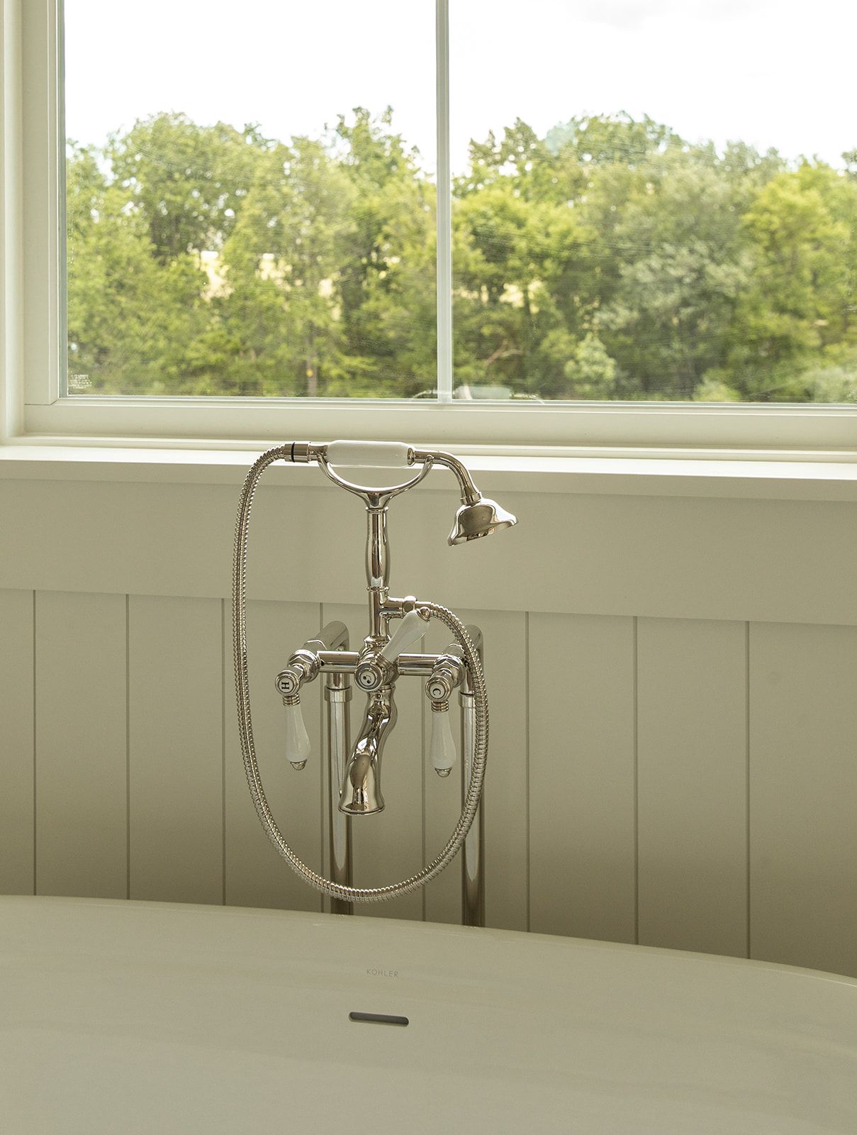 Elegant freestanding bathtub with polished nickel floor-mount faucet and hand shower beside a bright window.