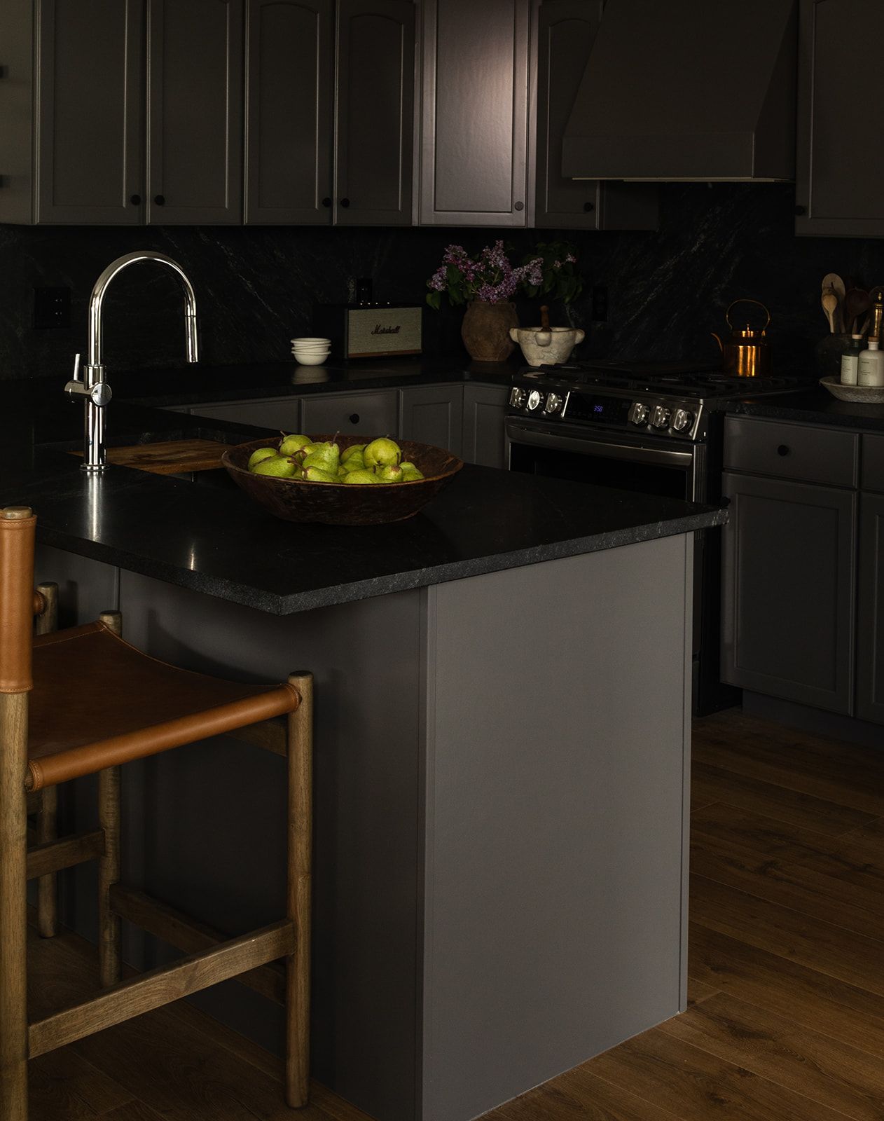 A modern dark wood and gray kitchen with black cabinets, hardwood flooring, and a sleek countertop island.