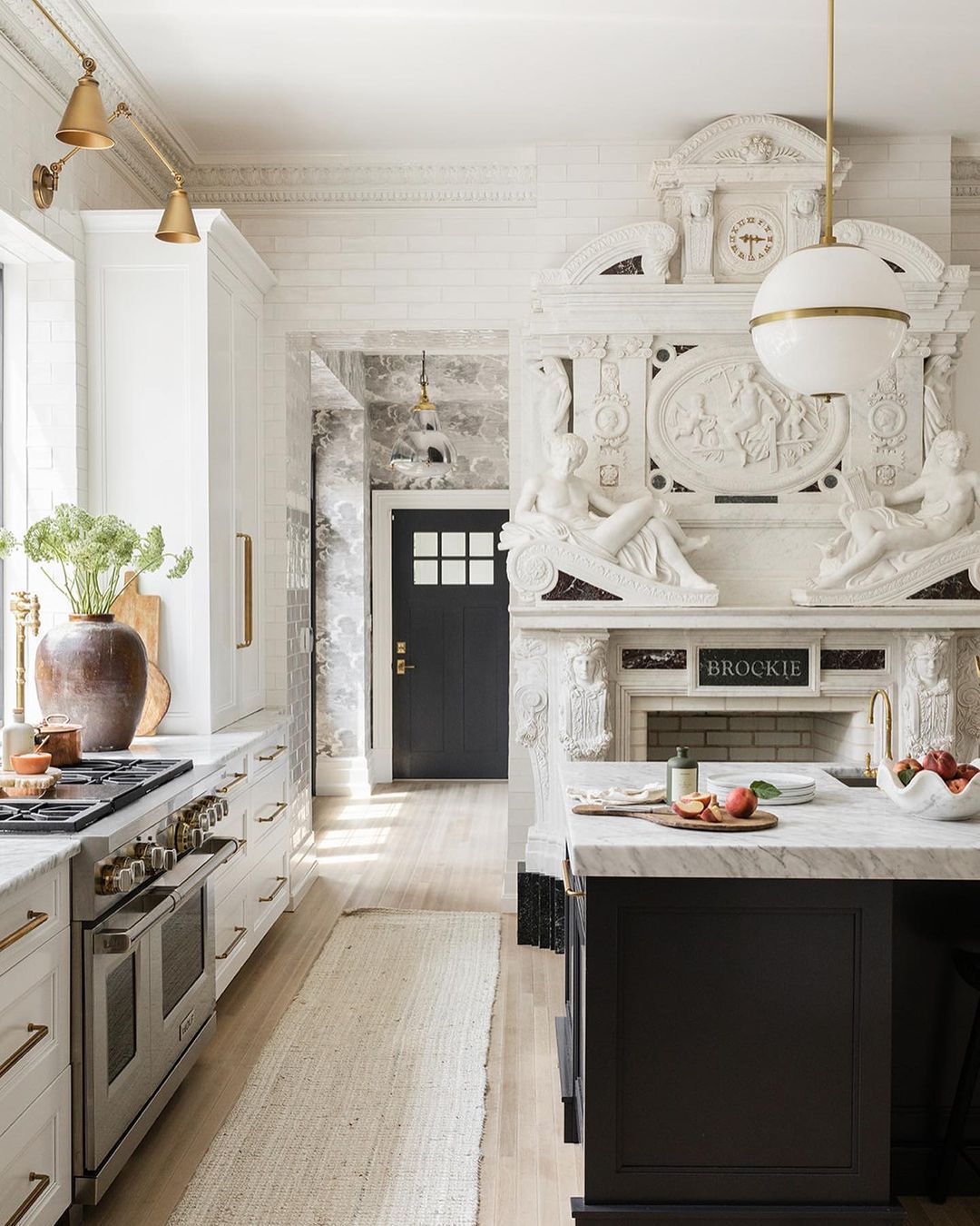 Modern white kitchen with contrasting dark cabinets, ornate wall reliefs, and gold pendant lighting above marble countertops.