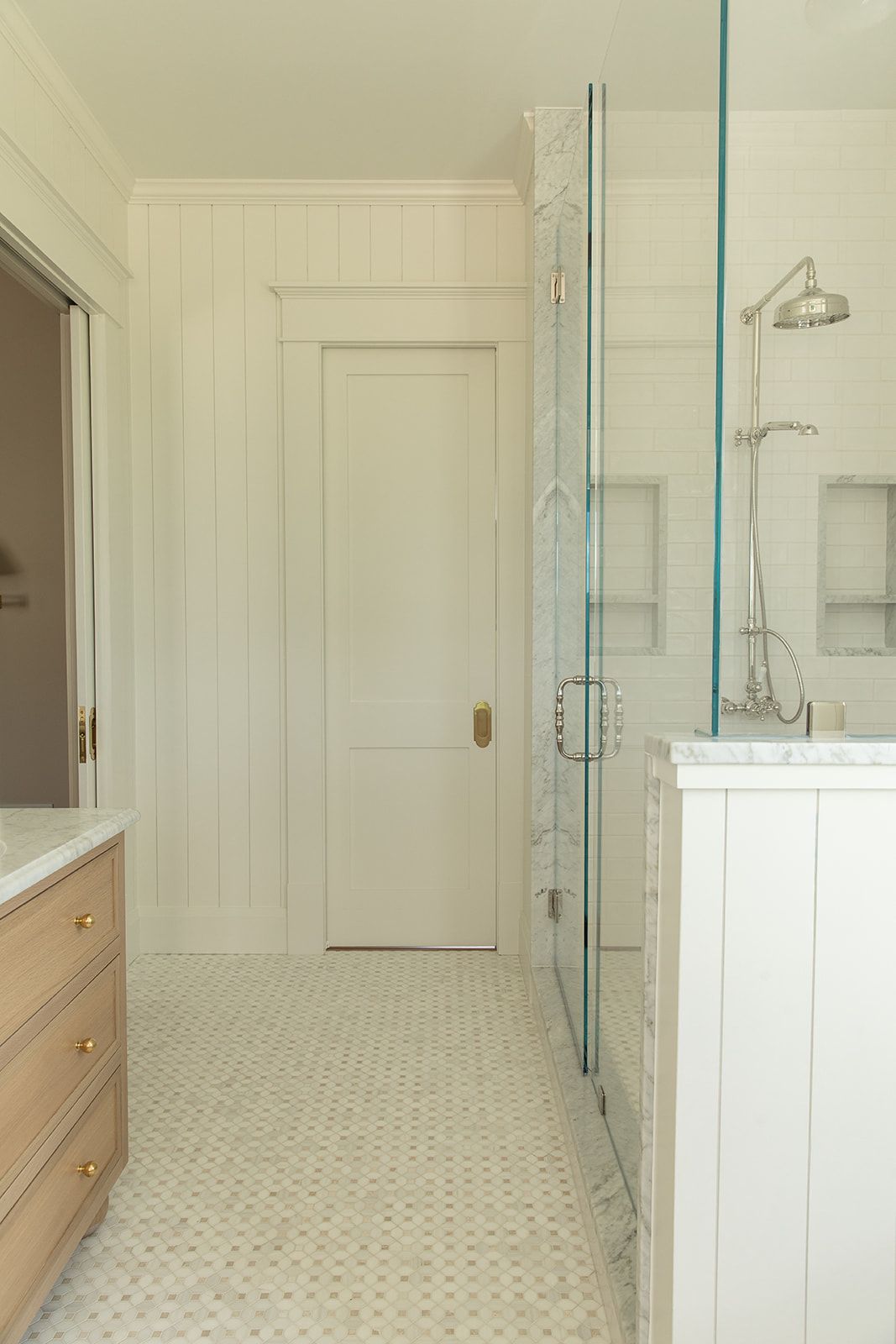 White bathroom with glass shower, penny tile floor, shiplap walls, marble countertop, and brushed nickel fixtures.