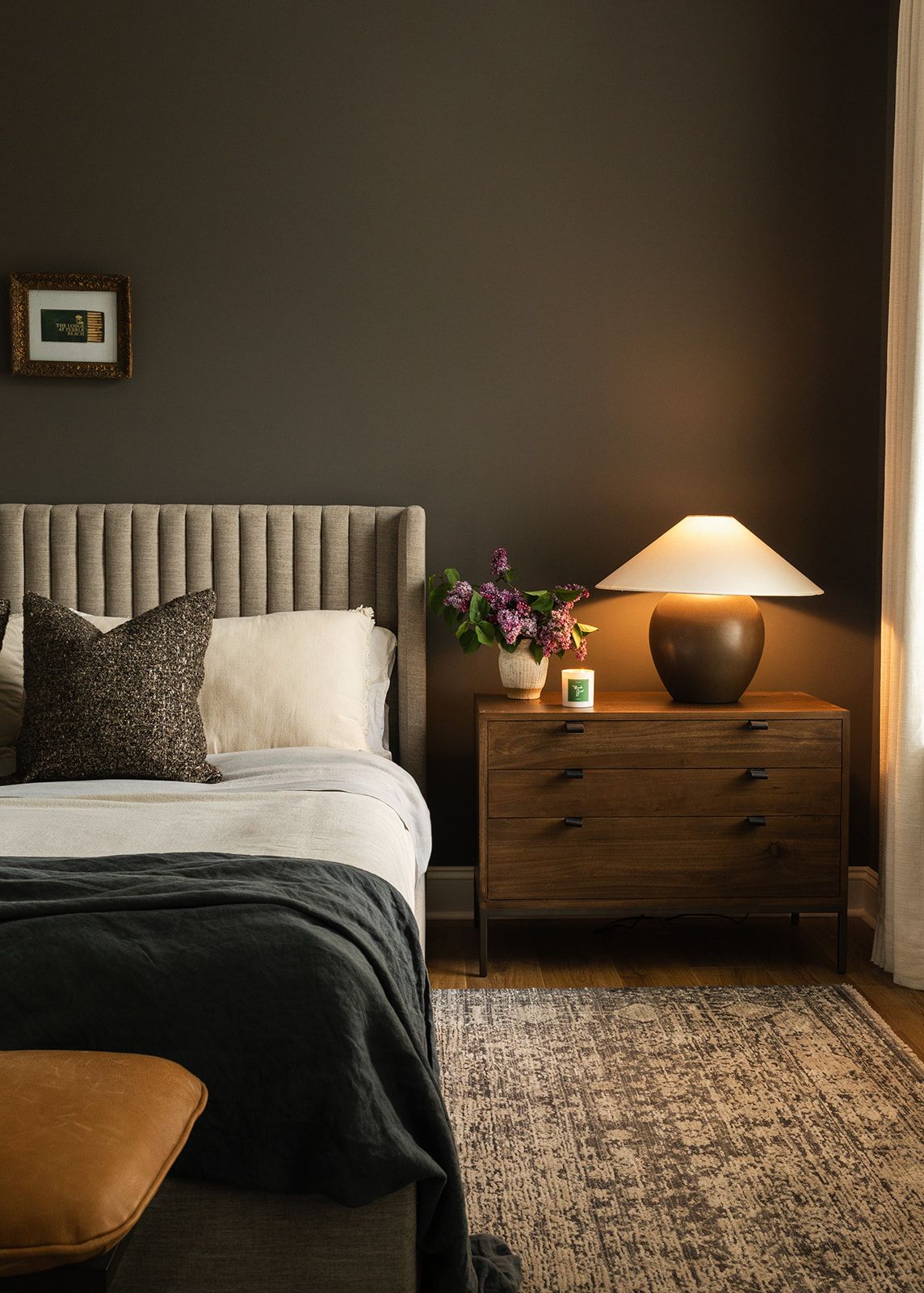 Contemporary bedroom interior with dark walls featuring a stylish wooden bed, bedside table, and textured area rug.