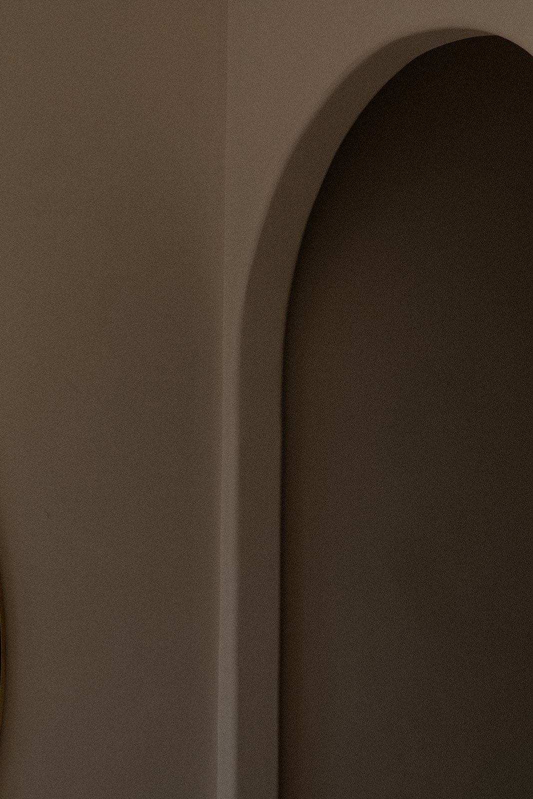 A minimalist architectural detail showing a curved archway with smooth white walls in dim lighting.