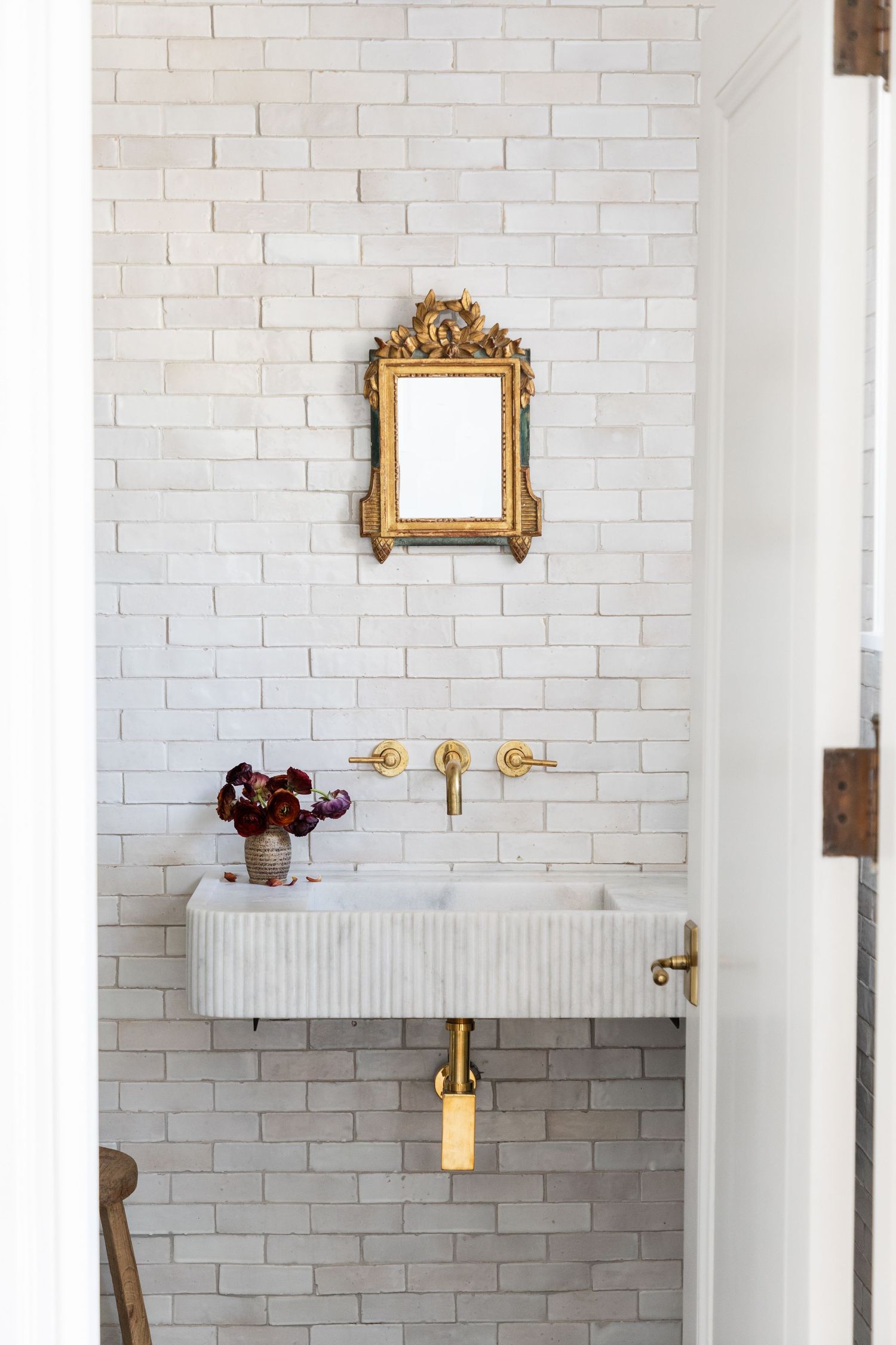 Minimalist bathroom featuring white subway tile, vintage gold mirror, and wall-mounted sink with brass fixtures.