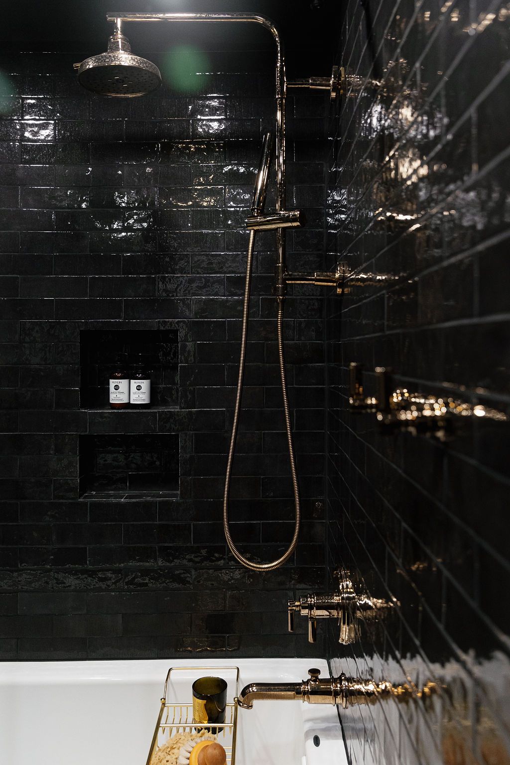 Modern bathroom with black tile walls features a sleek gold shower head and fixtures against dark minimalist design.