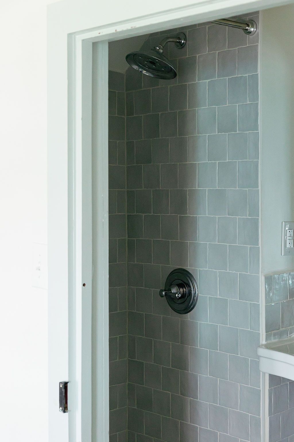 Modern bathroom shower enclosure with grey tile walls and black fixtures mounted against white walls.