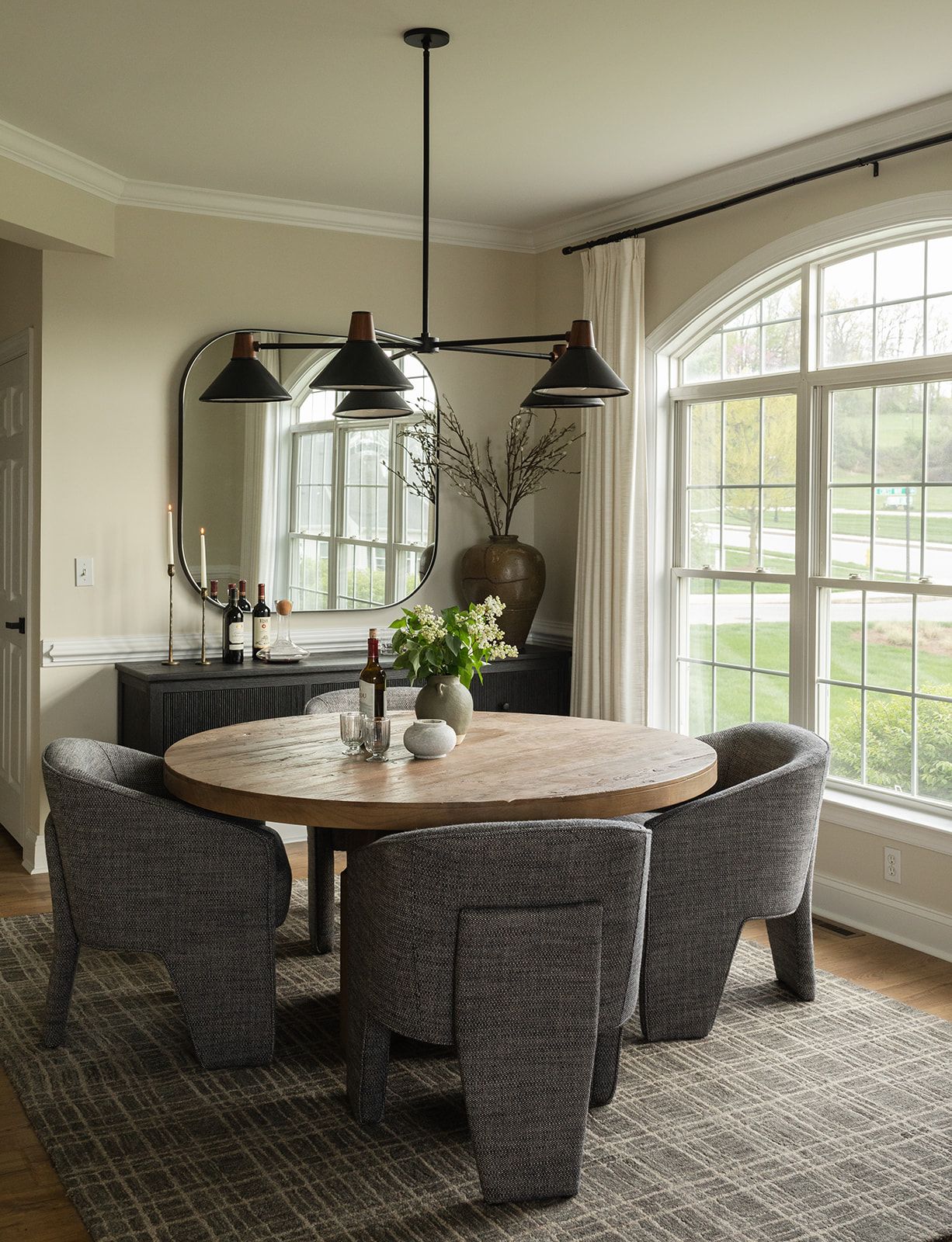 A modern dining room features a curved banquette seating arrangement around a round table with pendant lighting and large windows.