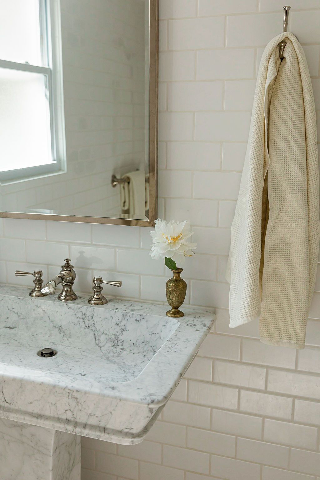 Elegant bathroom interior with marble countertop, vintage faucet, and white subway tile backsplash against bright window light.