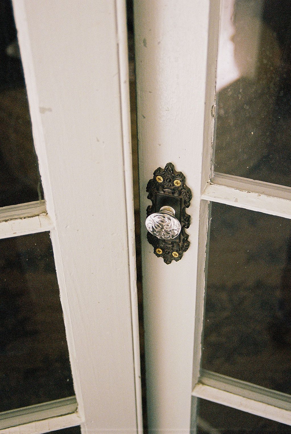 A vintage ornate ceramic doorknob with floral design mounted on white paned glass doors.