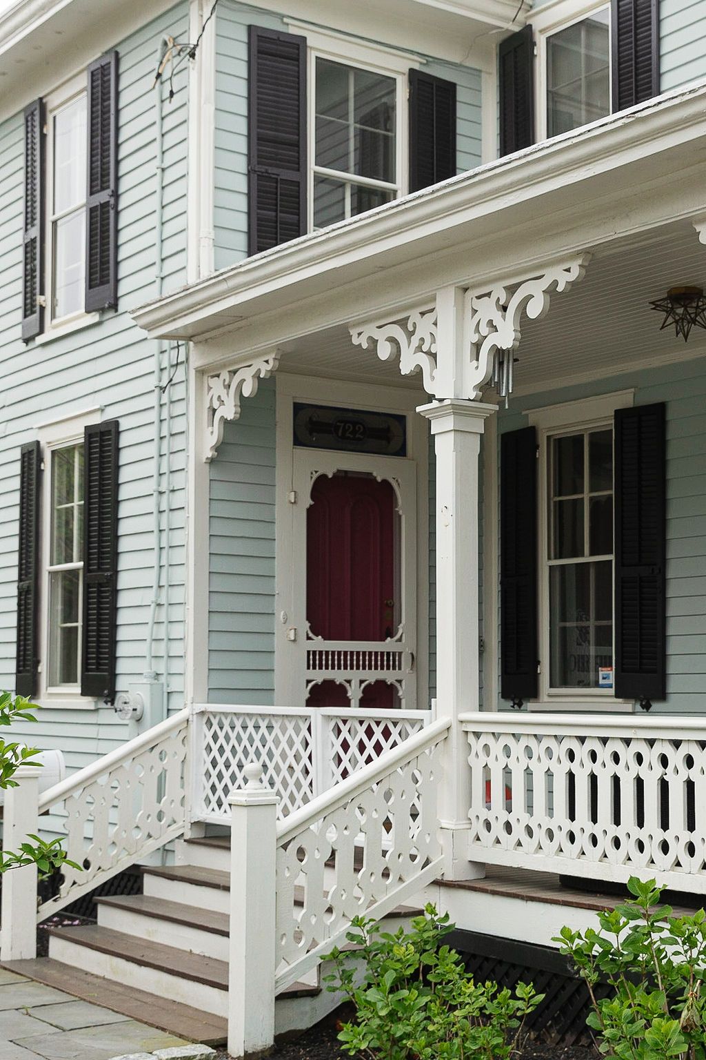Classic Victorian home entrance with white porch railings, ornate brackets, and burgundy screen door against pale blue siding.