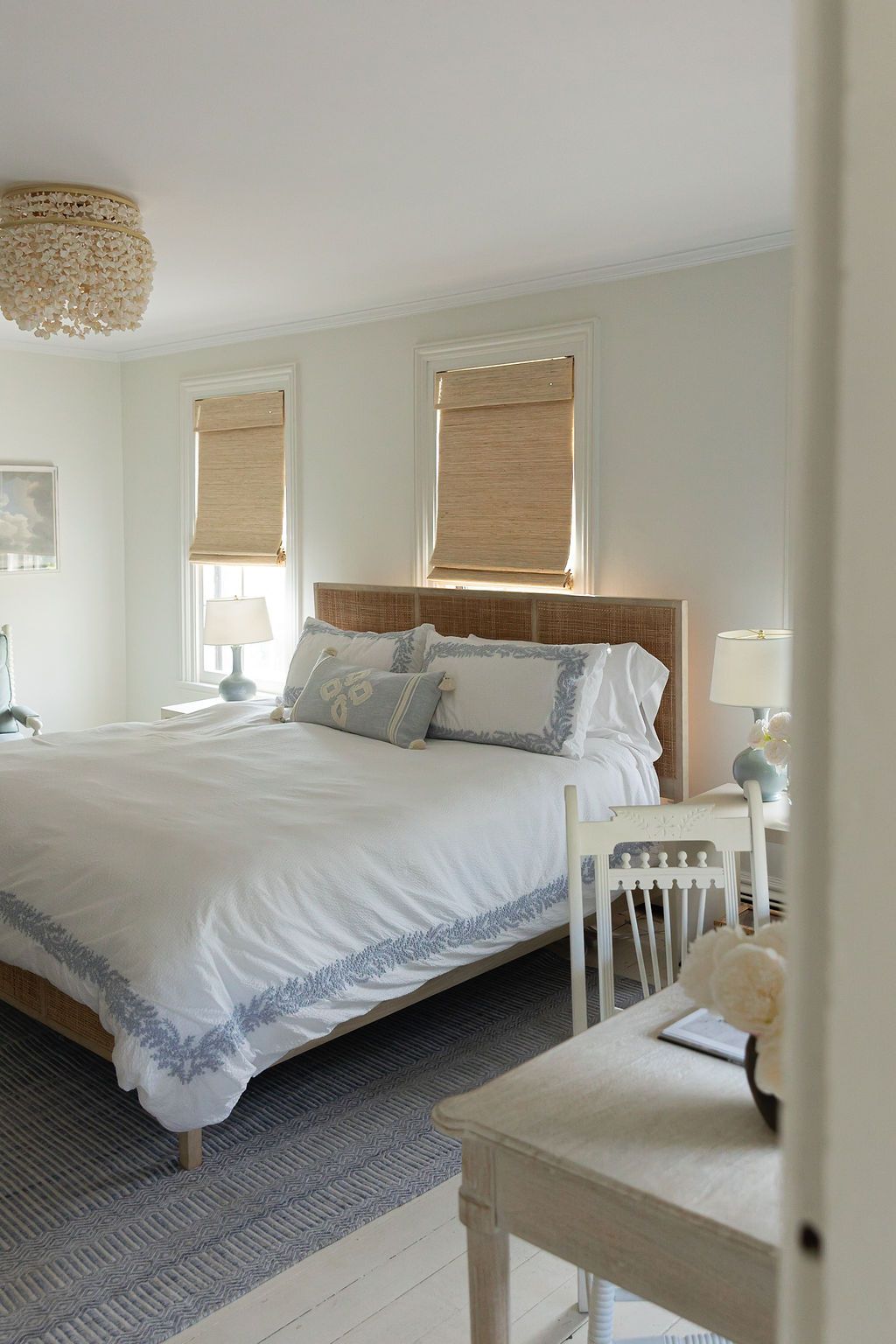 A serene modern bedroom with a wooden bed frame, white bedding, bamboo shades, and a beaded chandelier.