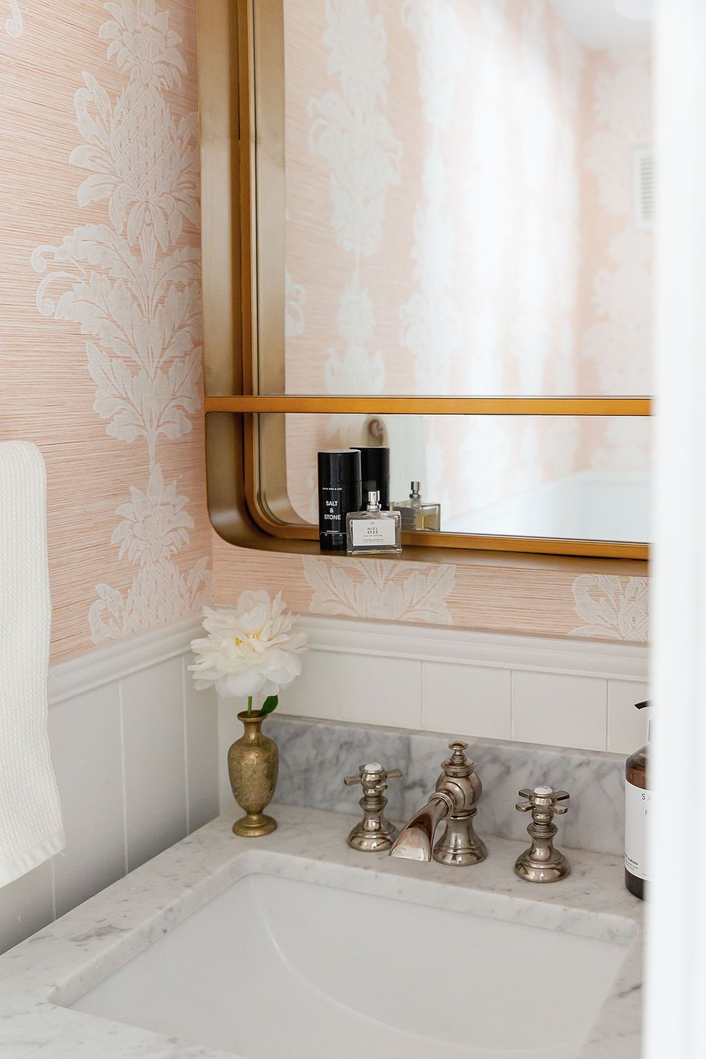 Elegant bathroom vanity with marble countertop, brushed nickel faucet, and peach floral wallpaper above white wainscoting.