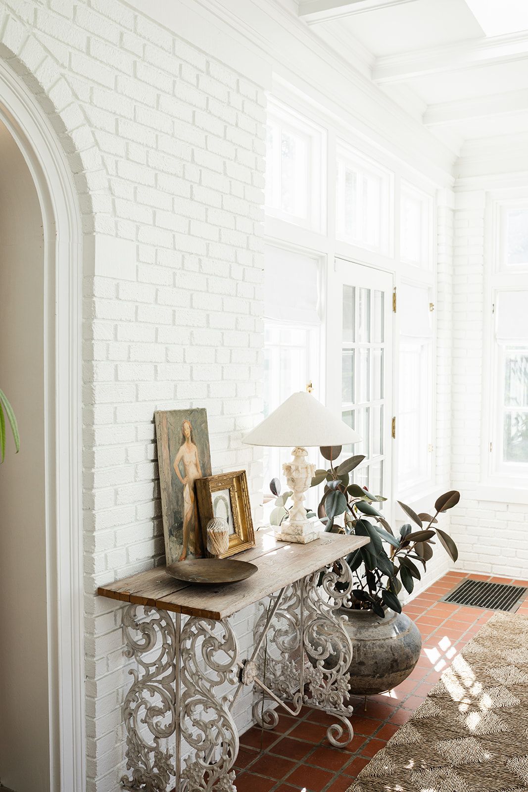 Elegant entryway with white brick walls and an ornate console table featuring vintage decor and potted plants.