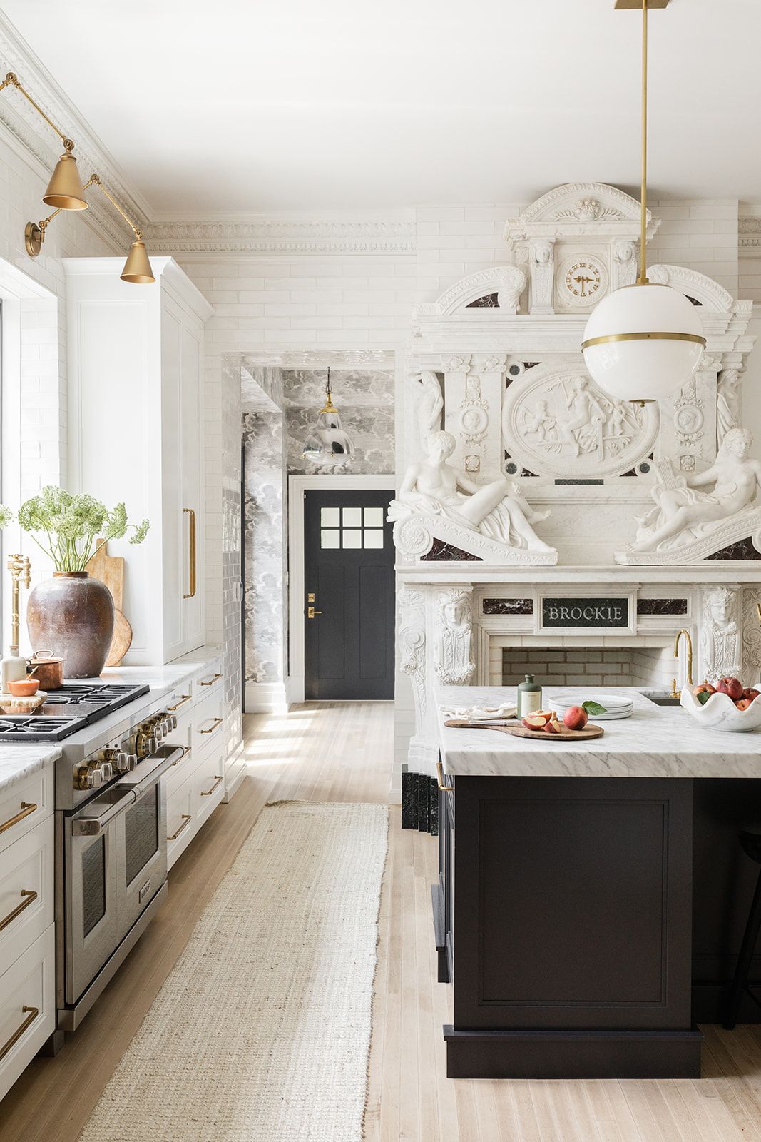 Bright kitchen interior with black island, white cabinets, and decorative marble fireplace.