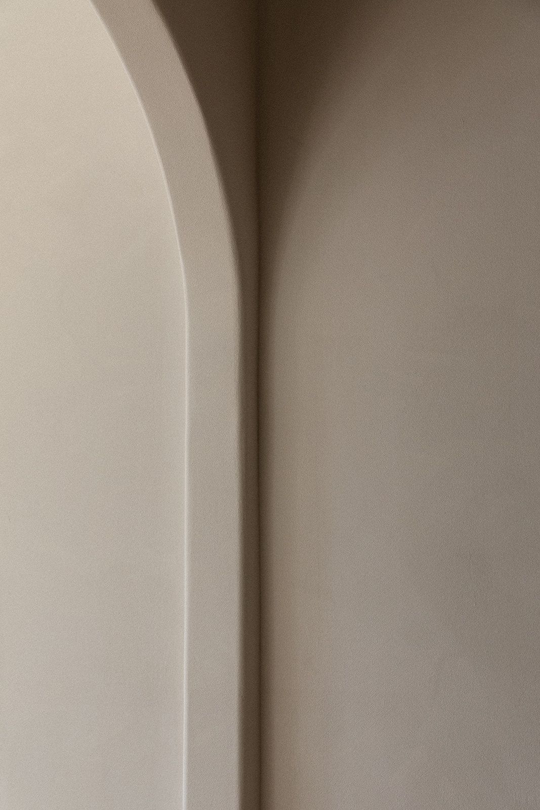 Minimalist architectural detail showing a smooth curved archway meeting a wall in soft beige tones.