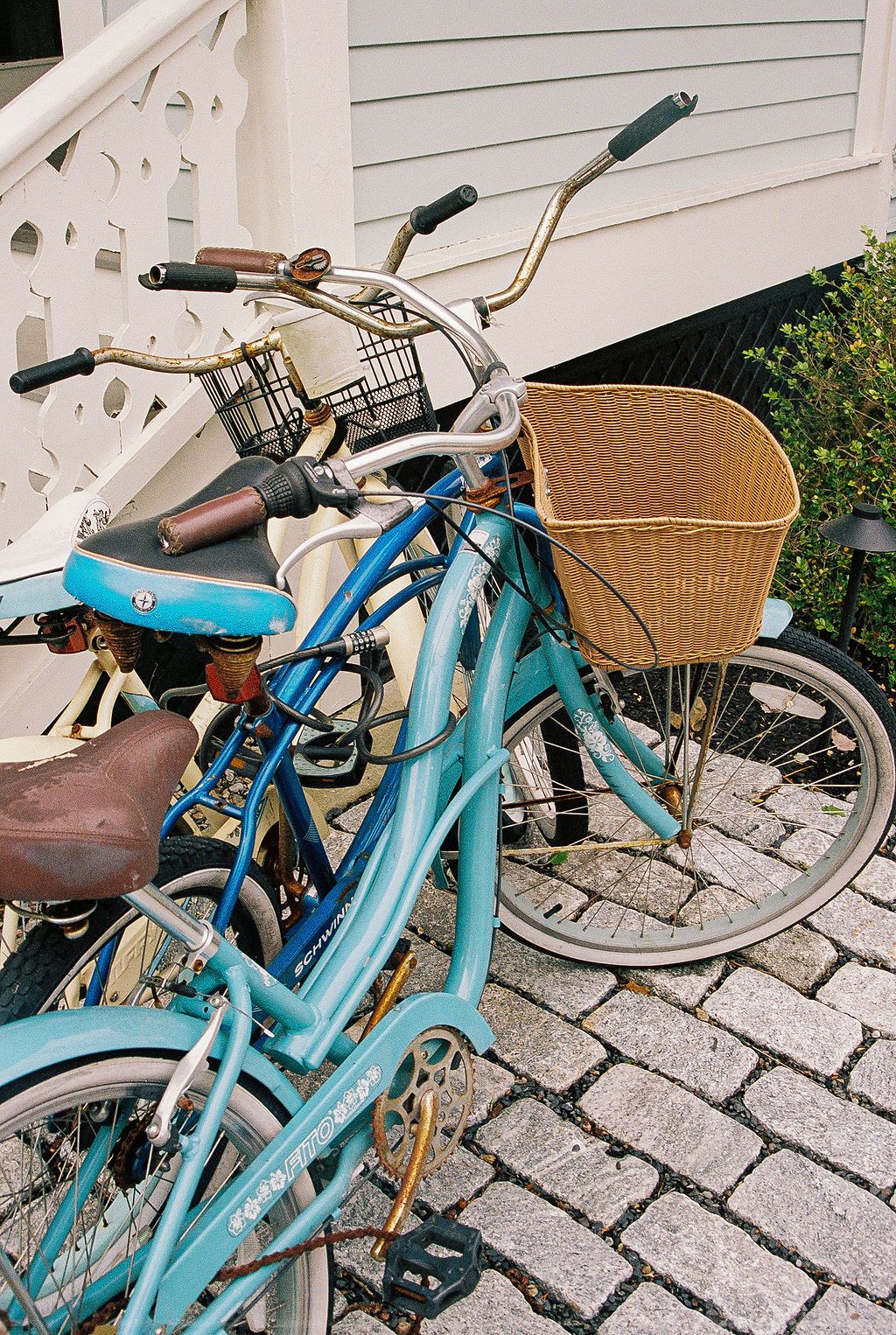 Vintage turquoise blue bicycle with wicker basket and silver handlebars parked on stone pavement in multiple angles.