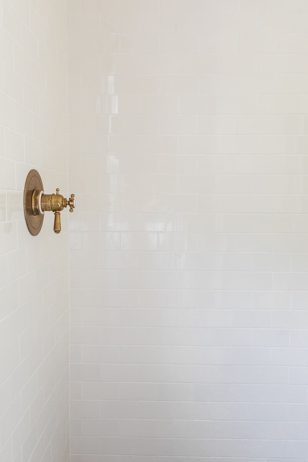 Vintage brass shower valve on glossy white subway tile wall in a clean modern bathroom.