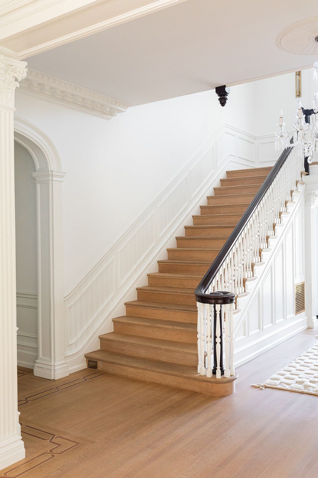 Traditional wooden staircase with white spindles and dark handrail in a bright foyer.