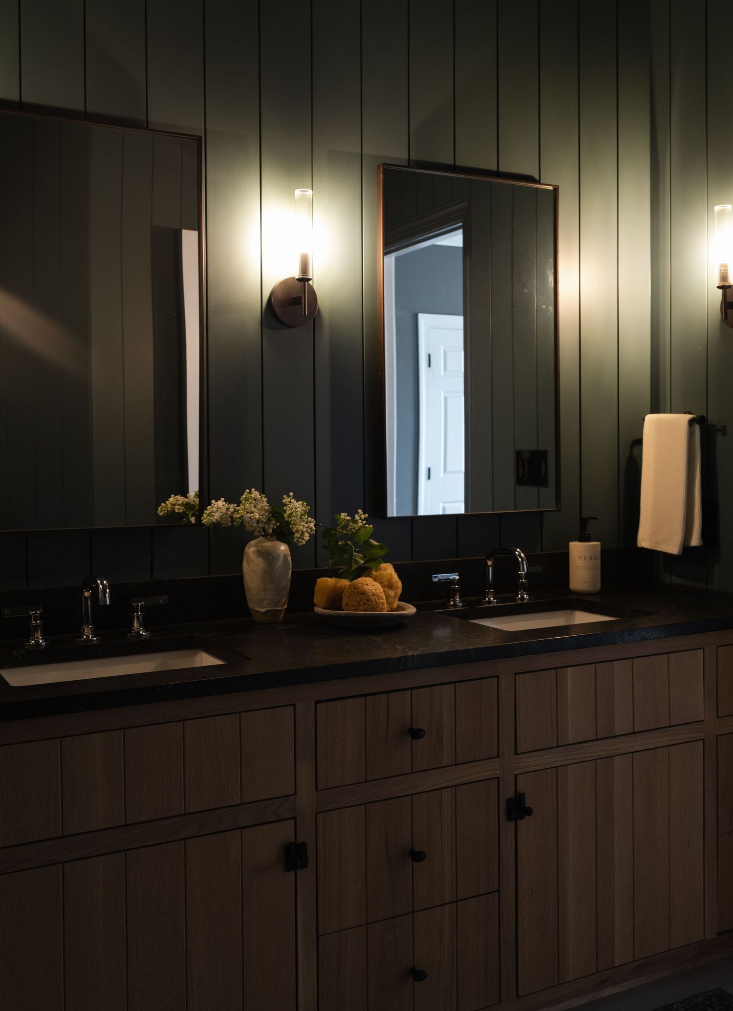 Dark modern bathroom vanity with vertical paneling, black cabinets, and moody lighting creating a dramatic atmosphere.
