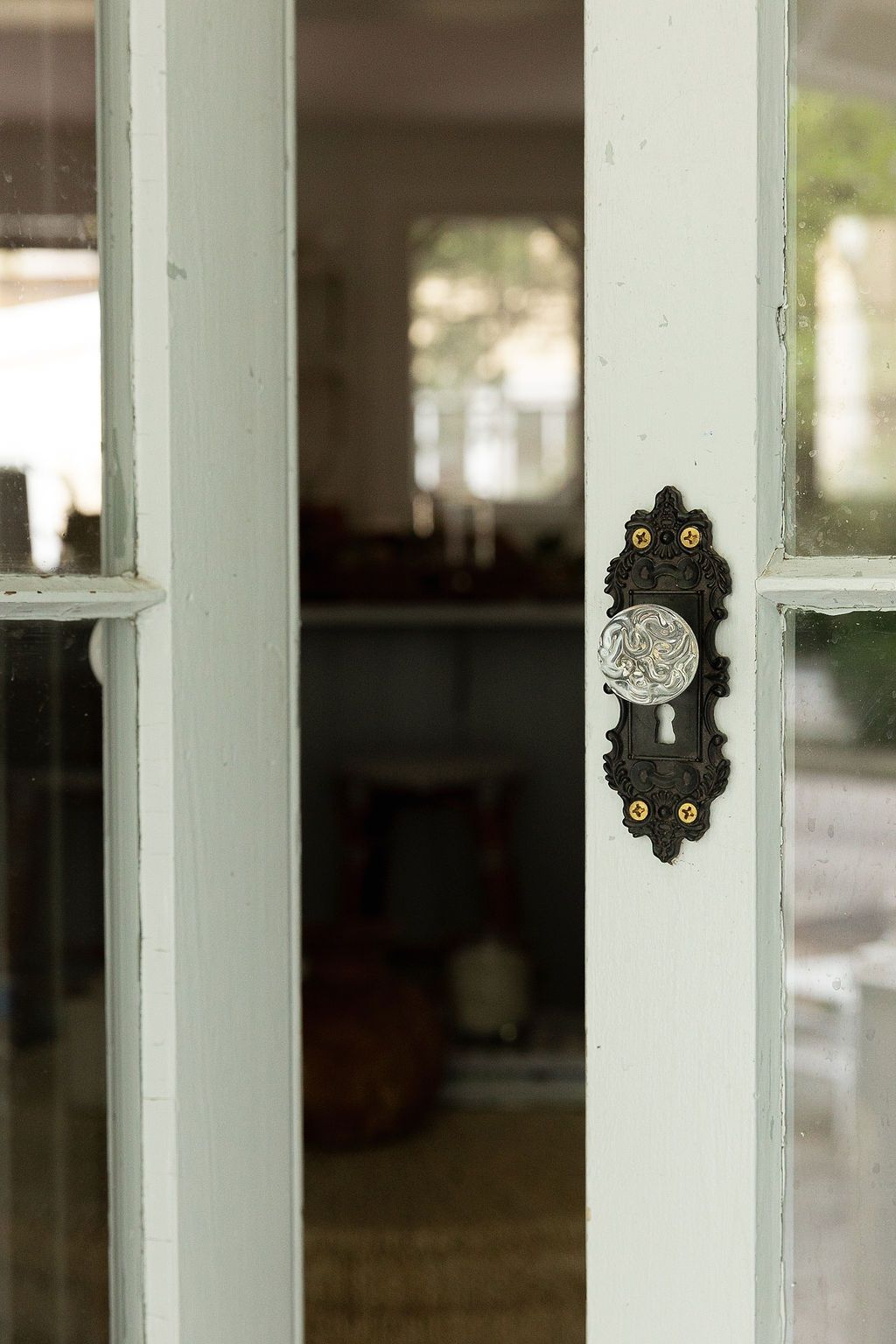 Vintage black door handle with ornate metal decorative plate mounted on a white-framed glass door.