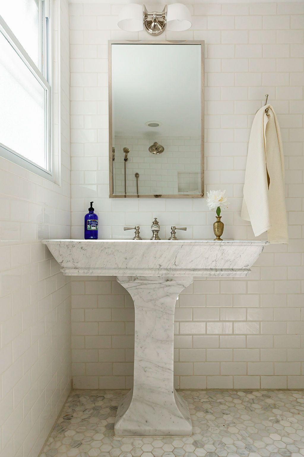 White marble pedestal sink against subway tile wall with pebble floor in bright minimalist bathroom setting.