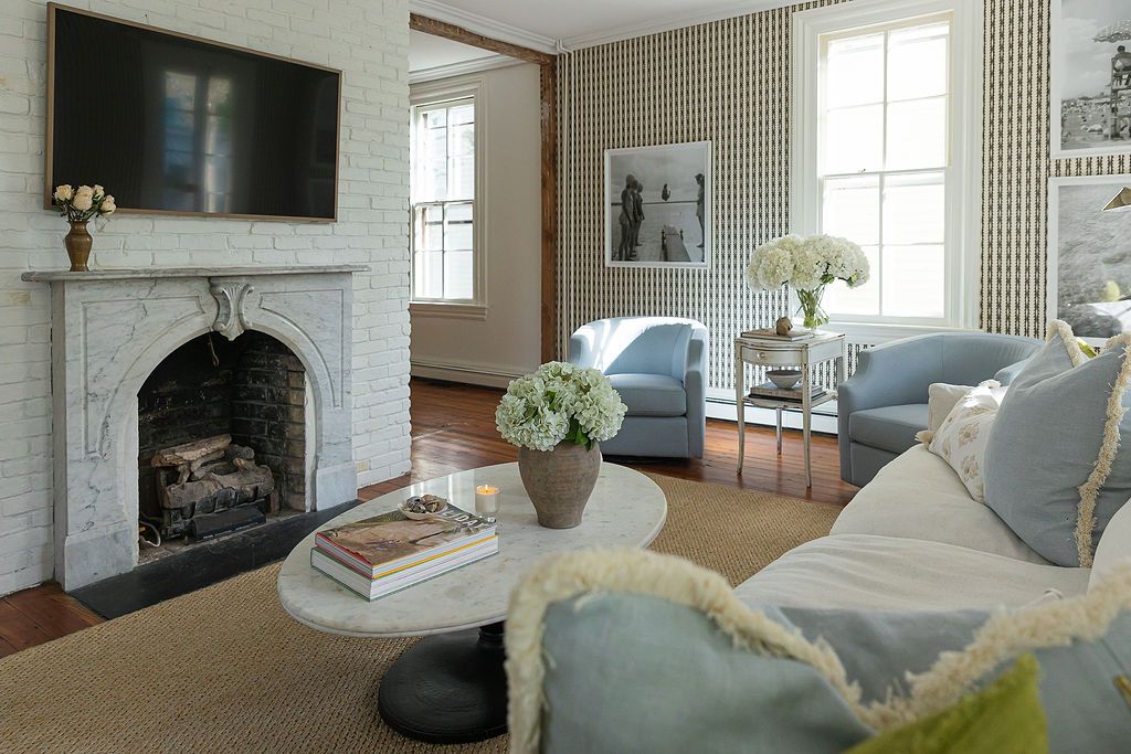 Elegant living room with marble fireplace, mounted TV, light blue armchairs, and checkered wallpaper in neutral tones.