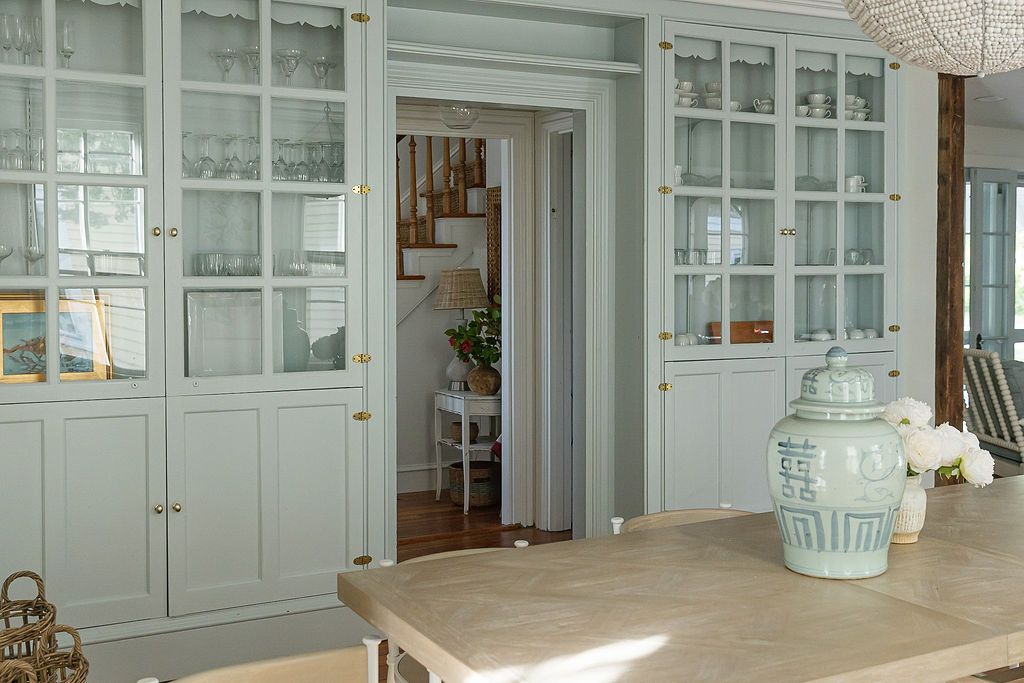 A luxurious white built-in cabinet system with glass doors spans the length of an elegant living room interior.
