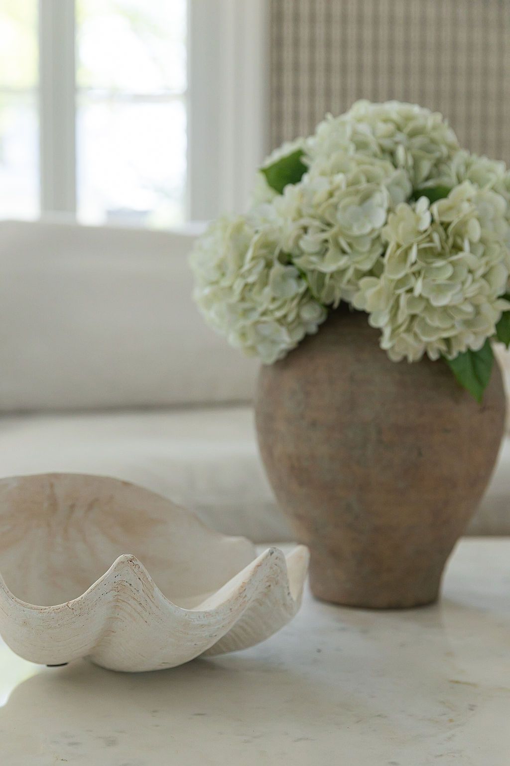White hydrangea flowers arranged in rustic brown pottery vases on a light windowsill.