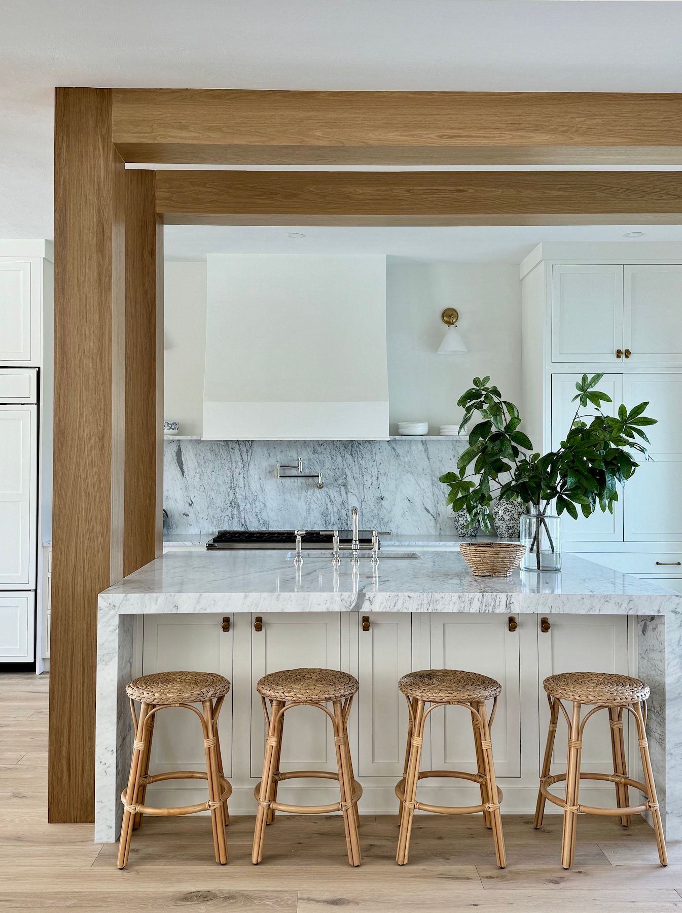 Sleek modern white kitchen with marble countertops and rattan bar stools arranged along a minimalist island.