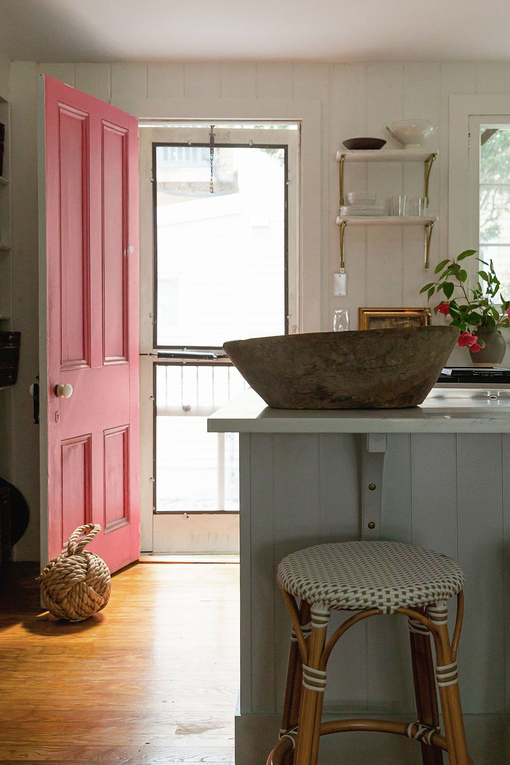 Modern kitchen interior with pink door and wooden floors features dark grey counters and rustic wood elements.