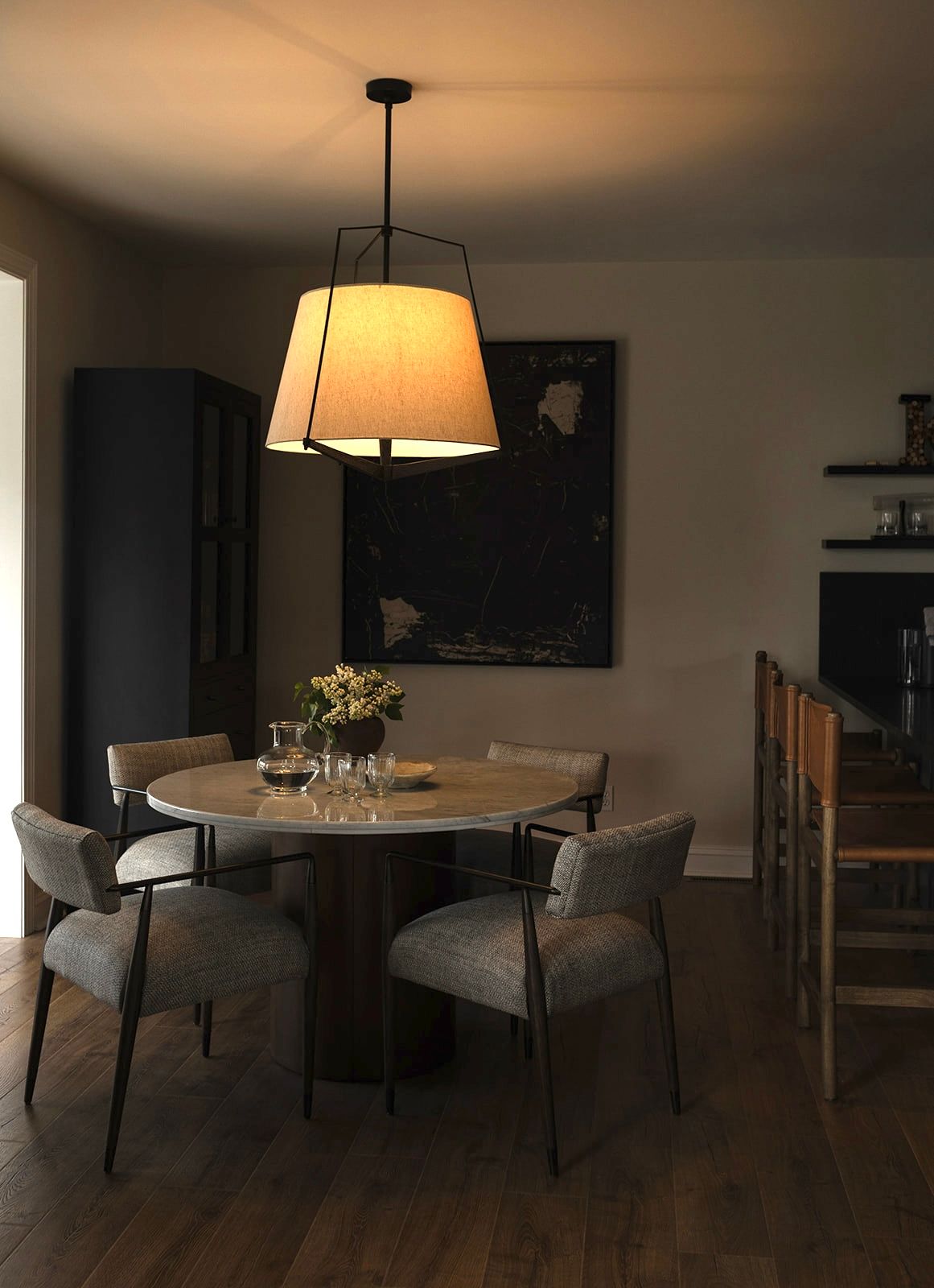 Modern dining area with round table, upholstered chairs, and pendant lighting in warm ambient setting.