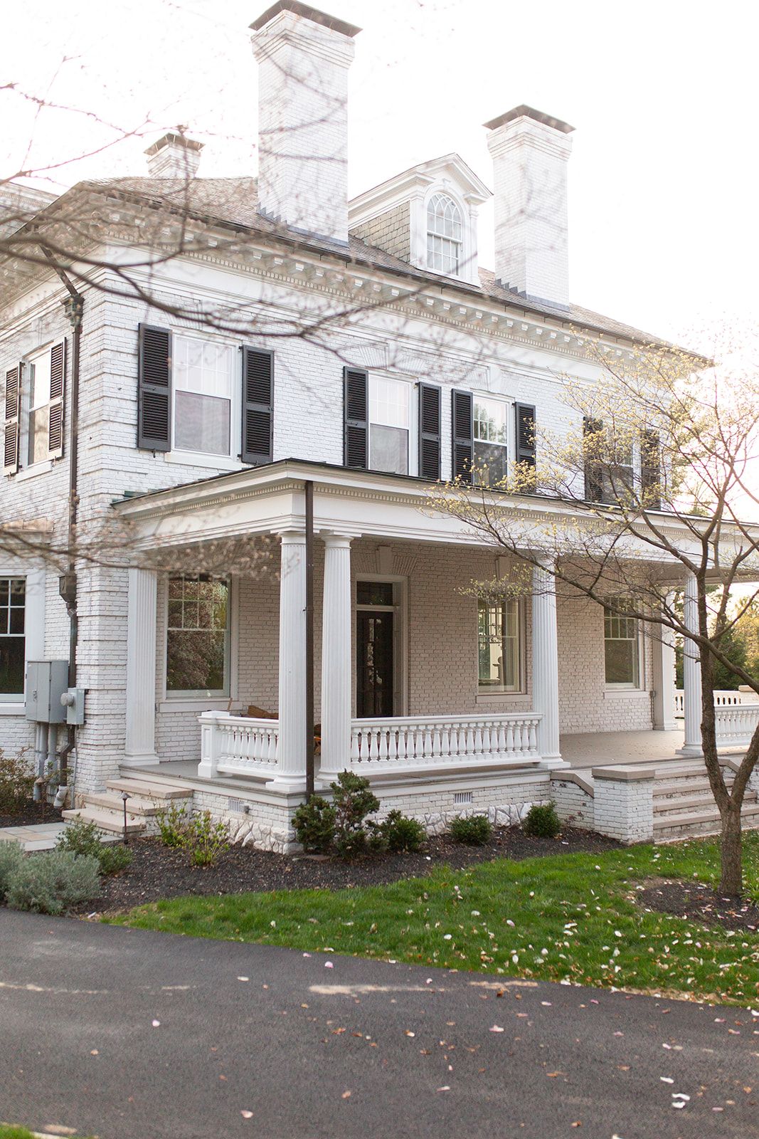 Classic white colonial house with black shutters and wraparound porch in winter.