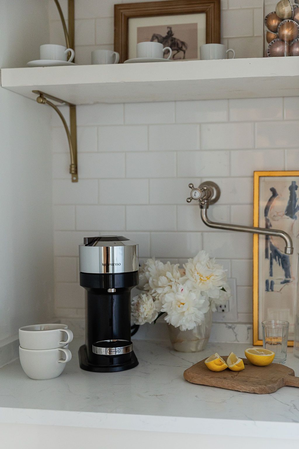 Kitchen counter display with coffee maker, white ceramics, cutting board, and citrus fruits against subway tile backsplash.