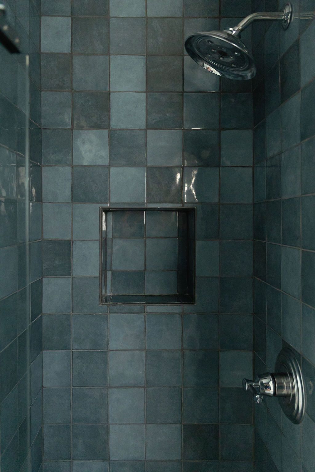 Modern bathroom interior with dark teal tiles, glass shower enclosure, and contemporary fixtures in a sleek design.
