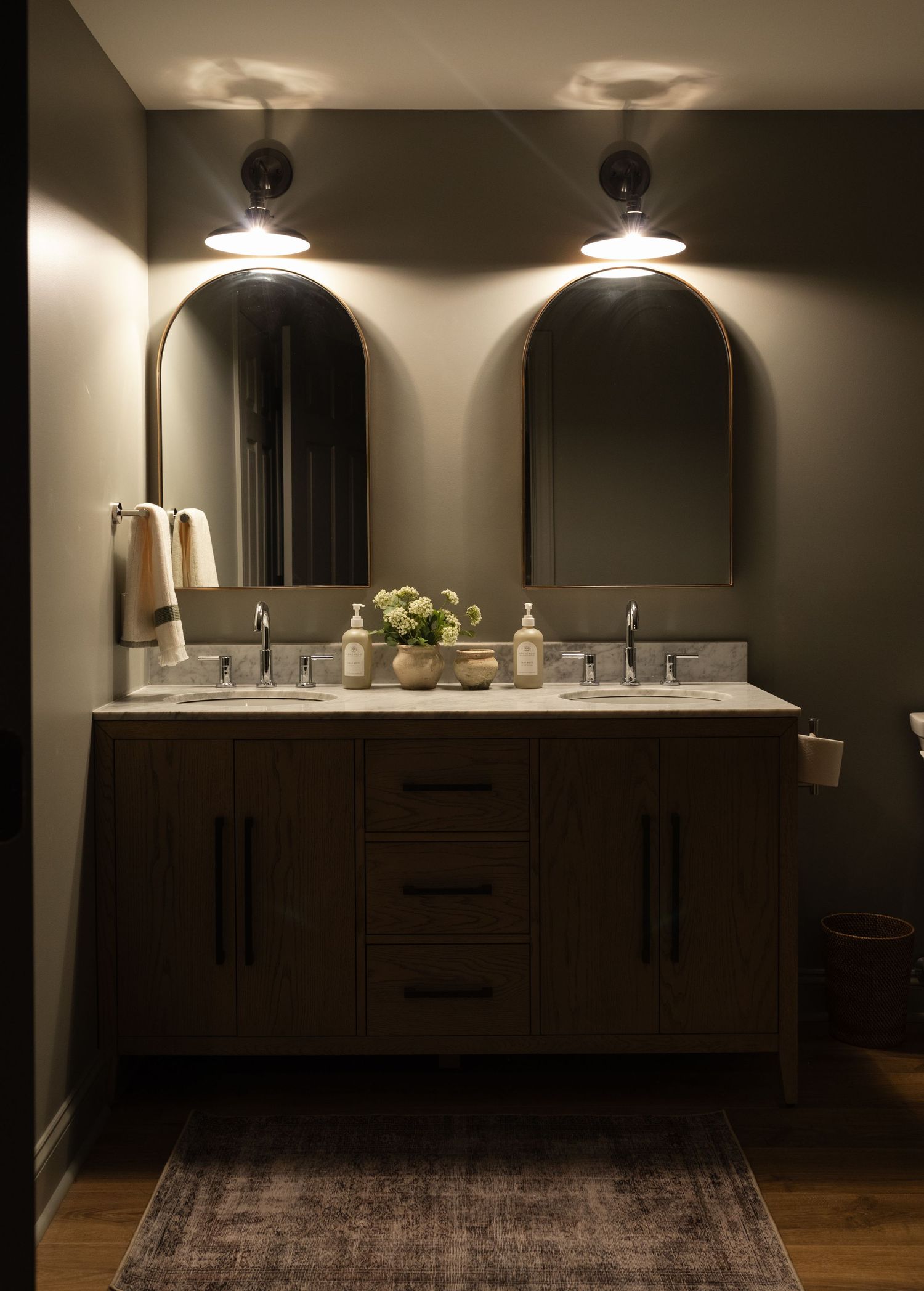 Modern bathroom vanity with dark wood cabinets, dual sinks, arched mirrors, and moody ambient lighting creates a luxurious feel.