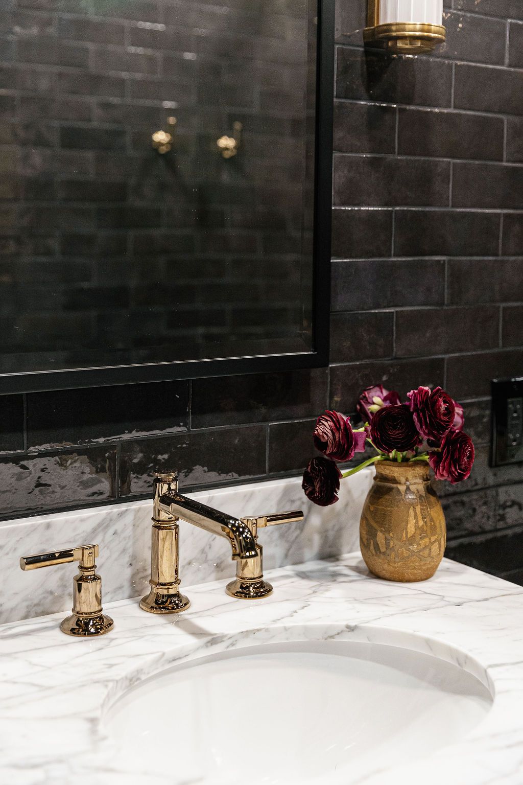 A luxurious brass bathroom faucet set against black marble and white countertop with burgundy roses in a gold vase.