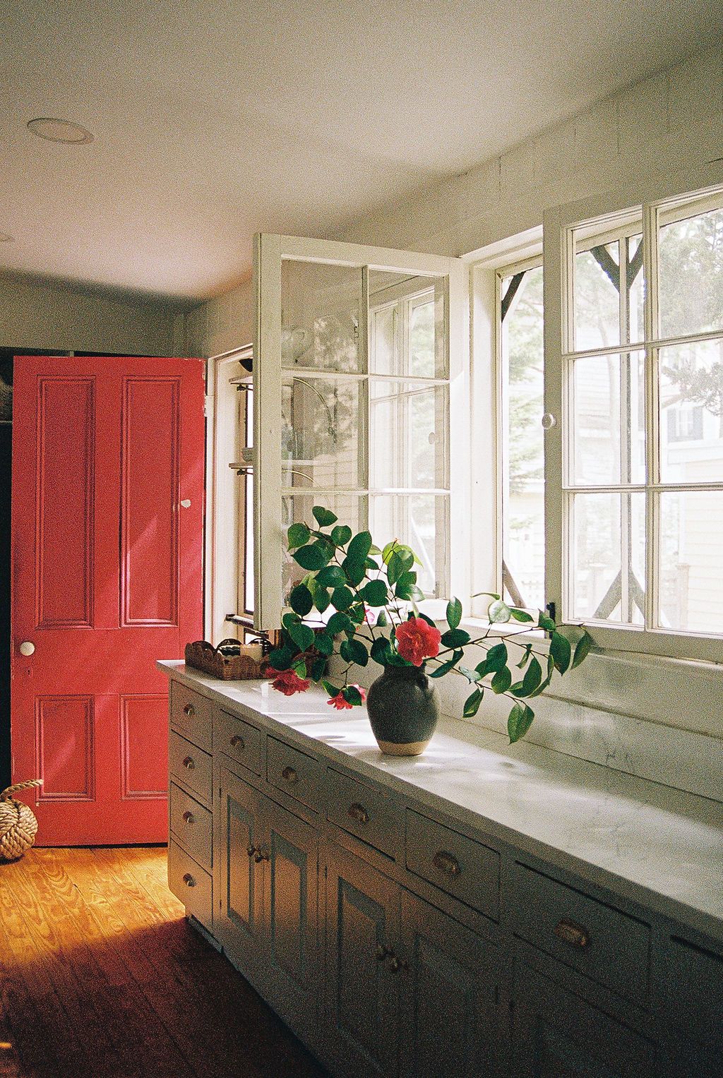 A bright red door anchors the end of a white hallway with built-in cabinets and natural light streaming through windows.