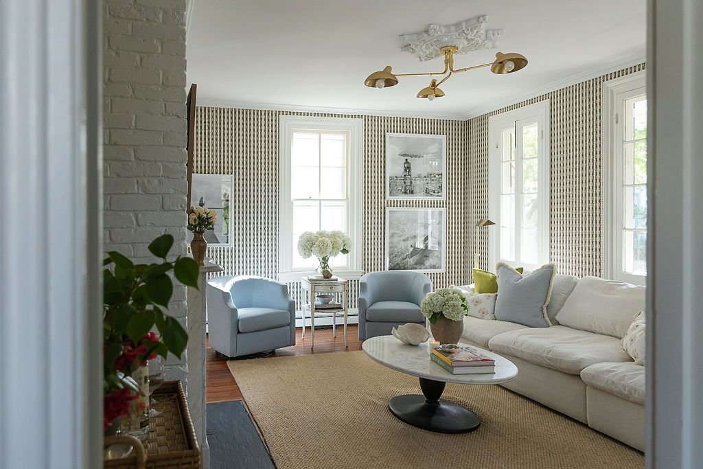 Modern coastal living room with white furniture, light gray walls, track lighting, and wraparound windows offering ocean views.