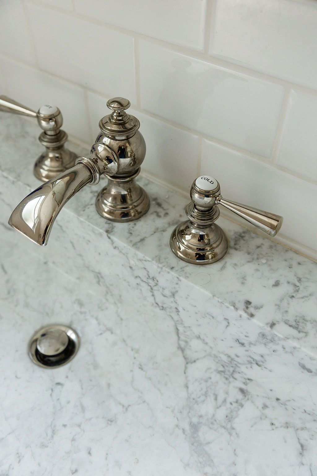 Close-up details of brushed nickel bathroom faucet fixtures with cross handles mounted on white marble countertop.