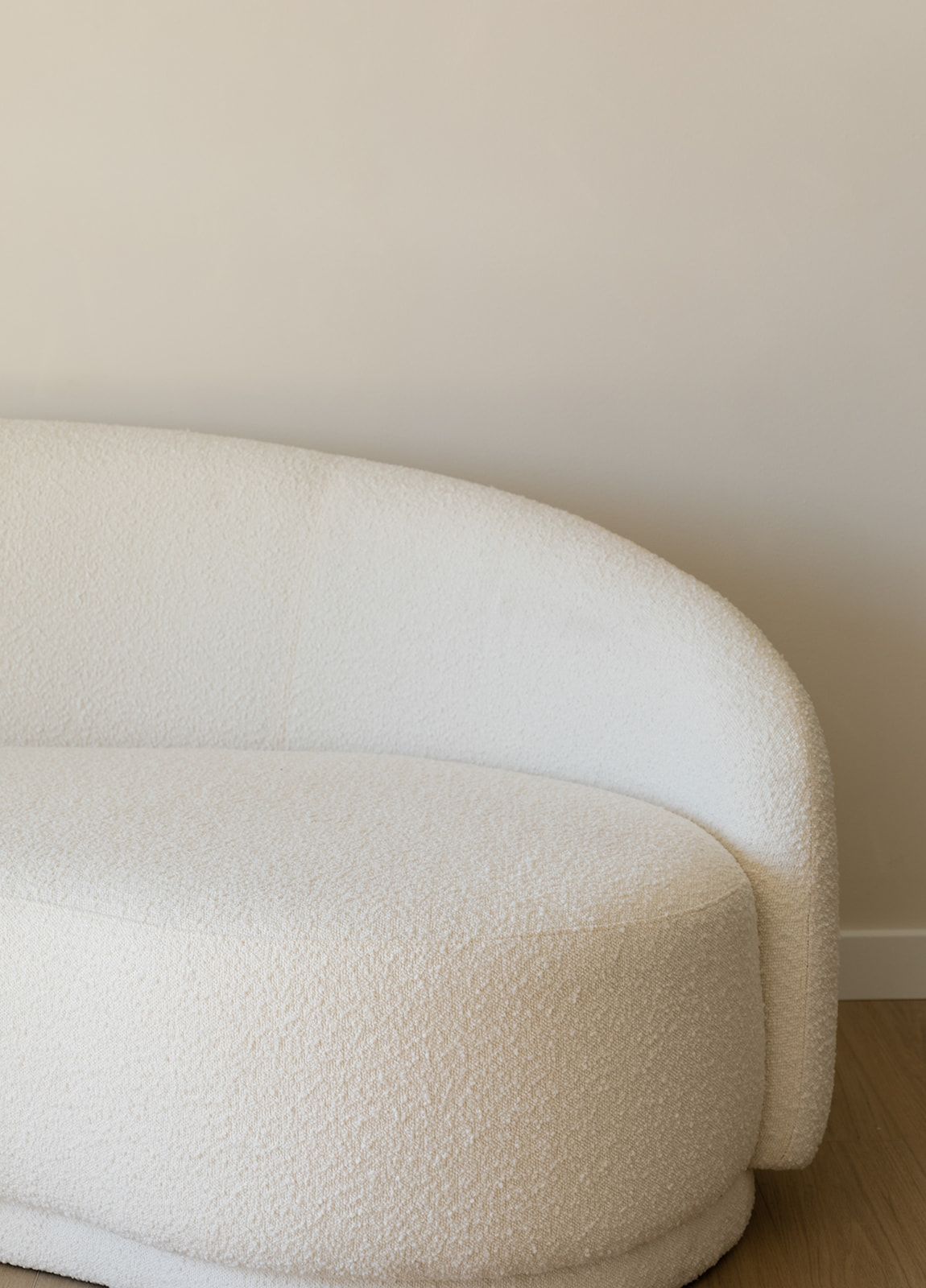 Close-up view of a curved white boucle chair with textured fabric against a neutral wall.
