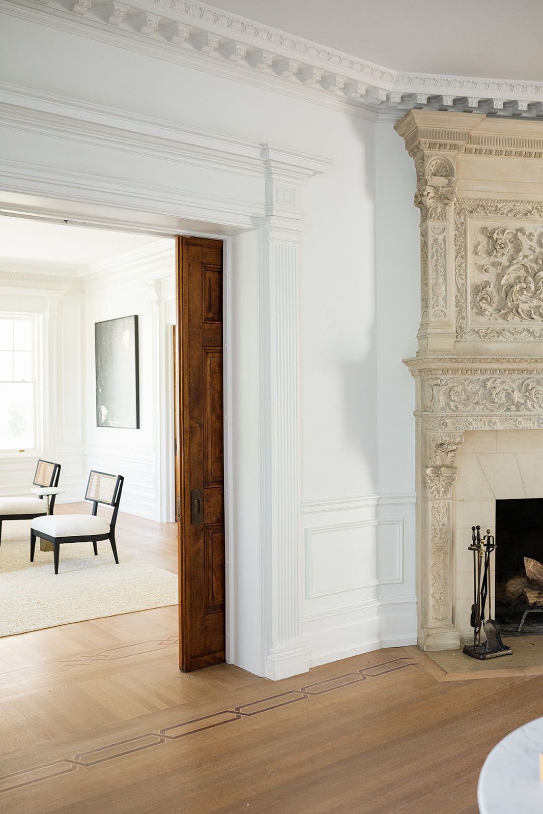 Elegant room with ornate crown molding, hardwood floors, and an elaborately decorated stone fireplace.