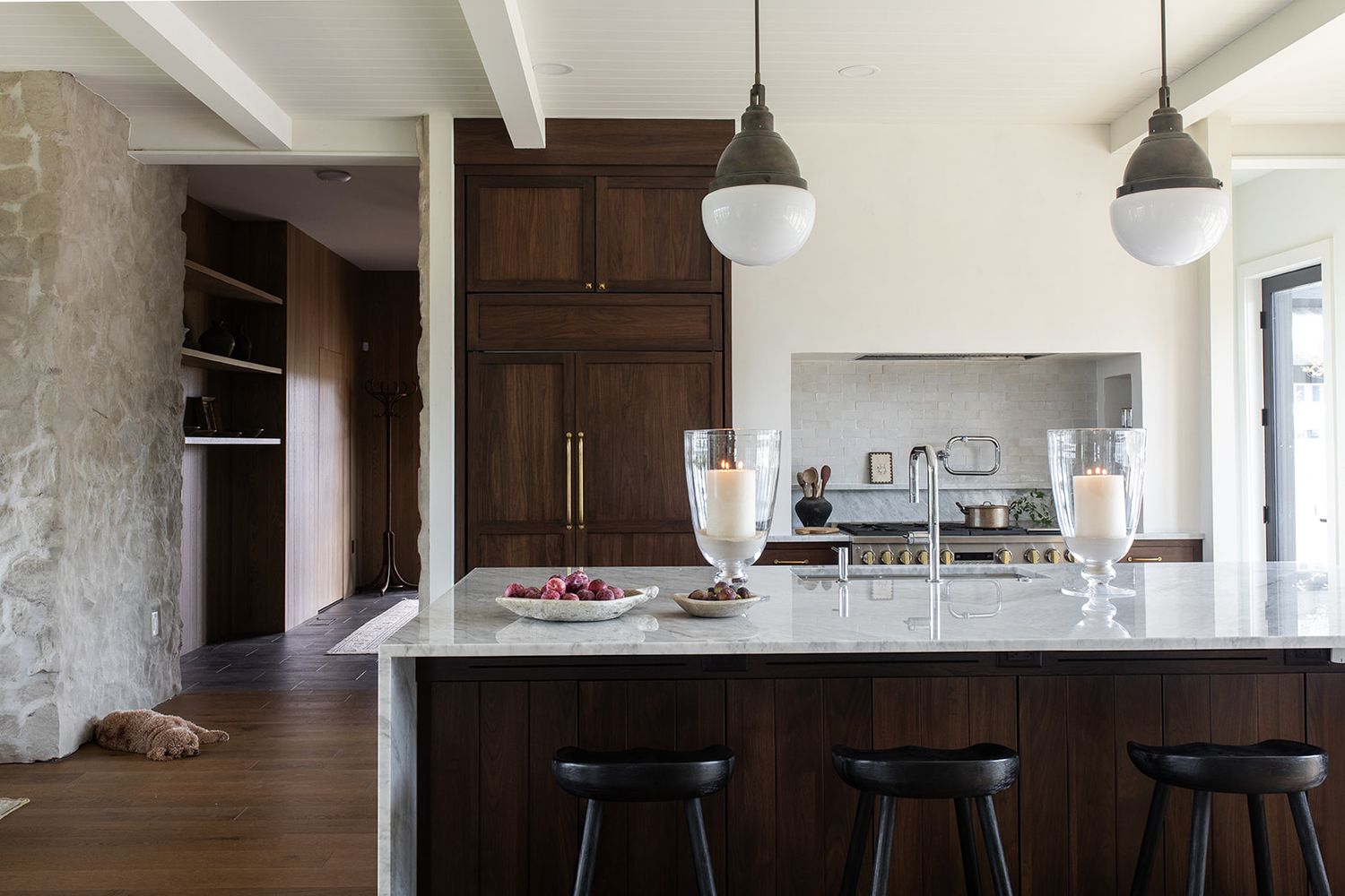 Modern kitchen with dark wood cabinets, marble island, black bar stools, and pendant lights over a spacious open layout.