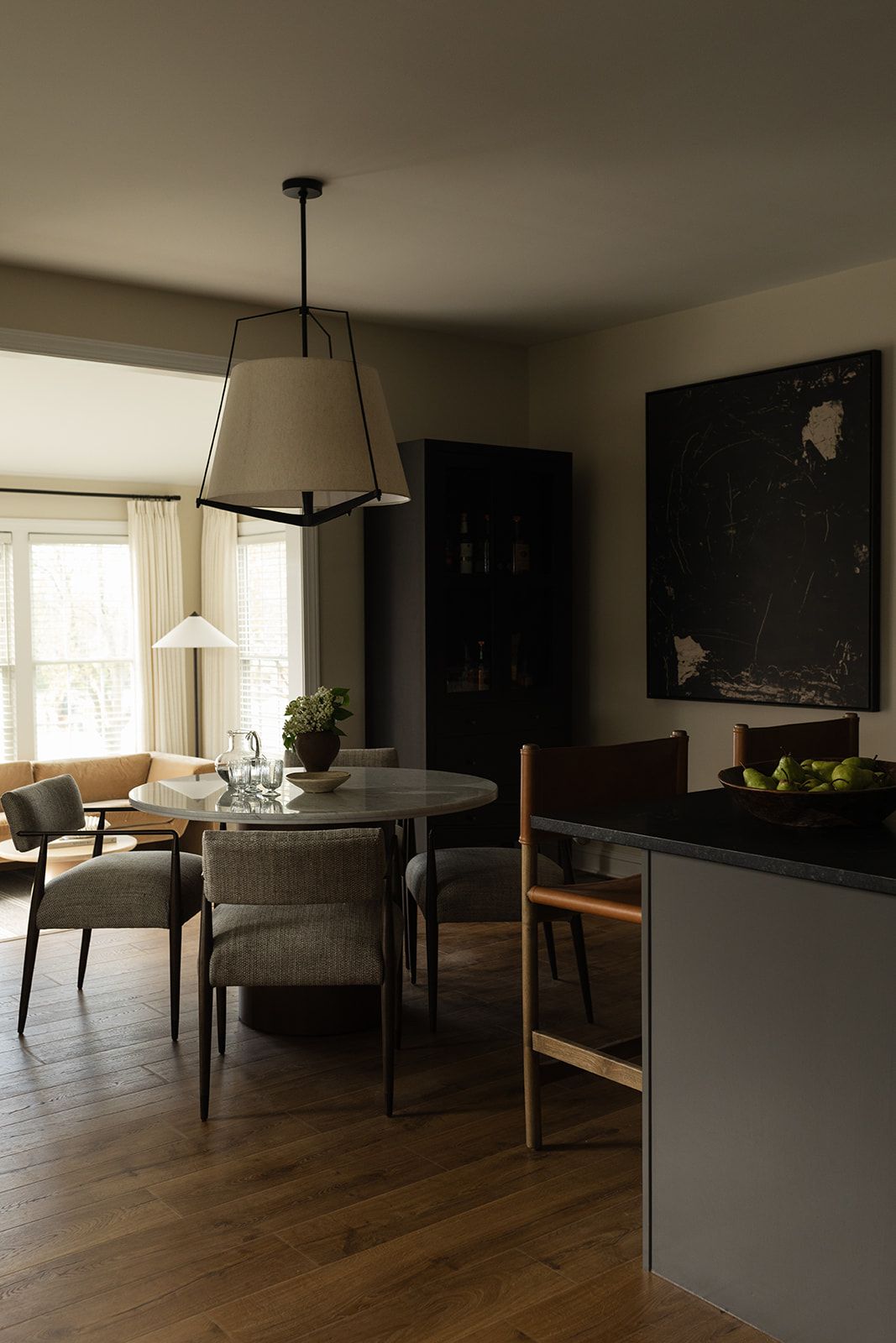 Modern living room and dining area with wooden floors, gray furniture, and natural lighting through large windows.