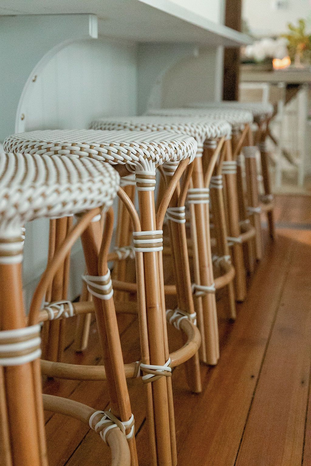 Row of rattan and bamboo bar stools with woven seats lined up at a kitchen counter.