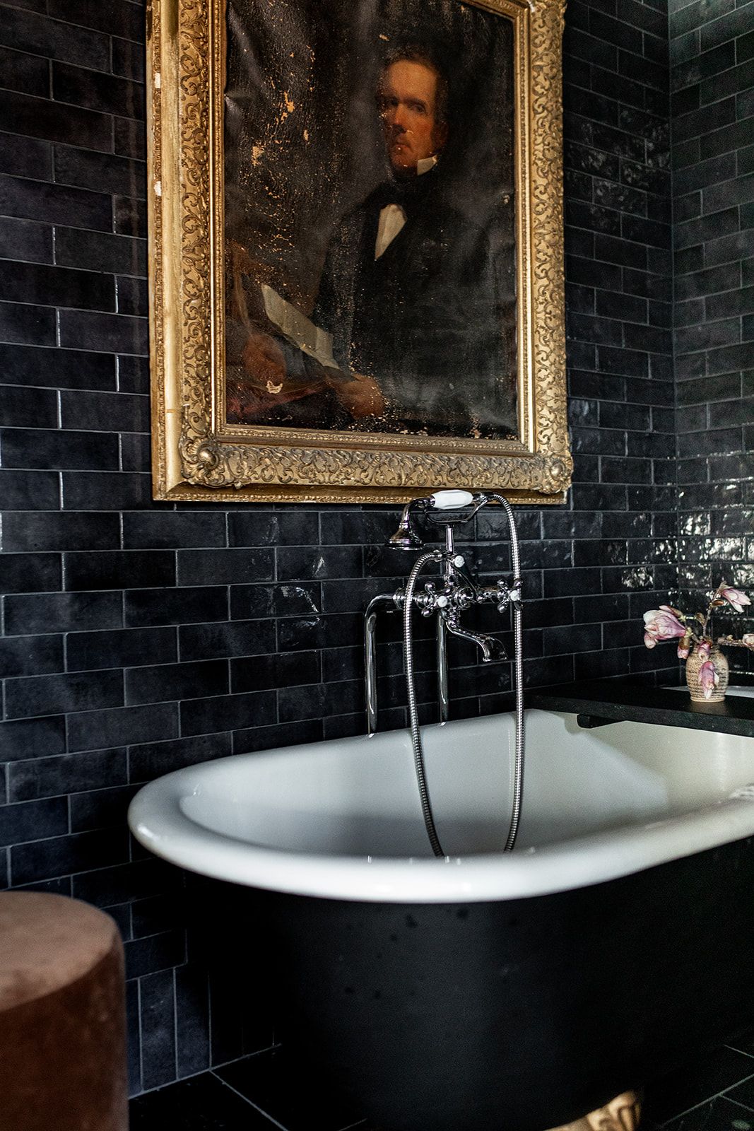 Victorian-style bathroom featuring black clawfoot tub, vintage artwork, and dark tiled walls.